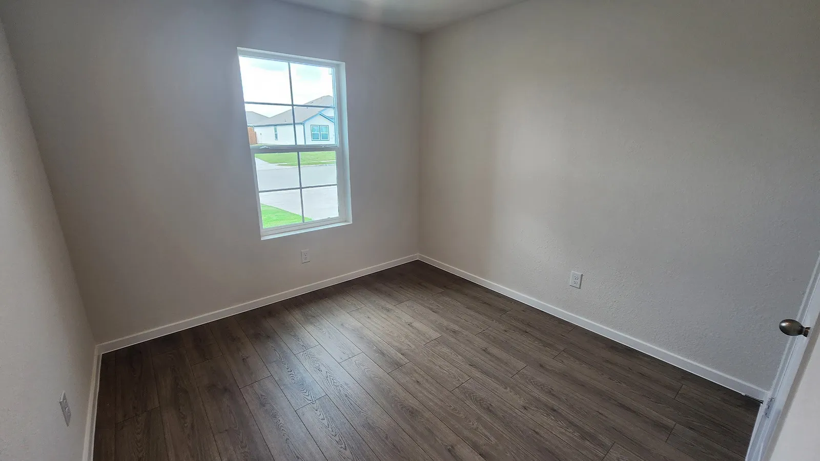 Room featuring wood-finish flooring, neutral wall tones, white baseboards, and a multi-pane window