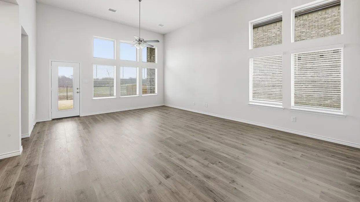 Spacious living area featuring high vaulted ceilings, light wood-finish flooring, a contemporary ceiling fan, and multiple large windows with horizontal blinds