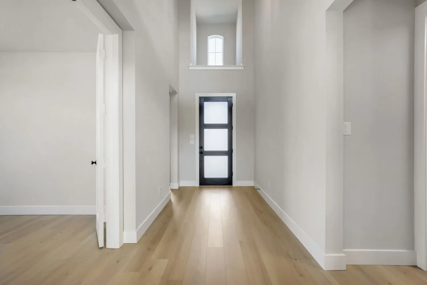 Light wood-finish flooring, high ceilings, contemporary black door with frosted glass panels, and a high transom window
