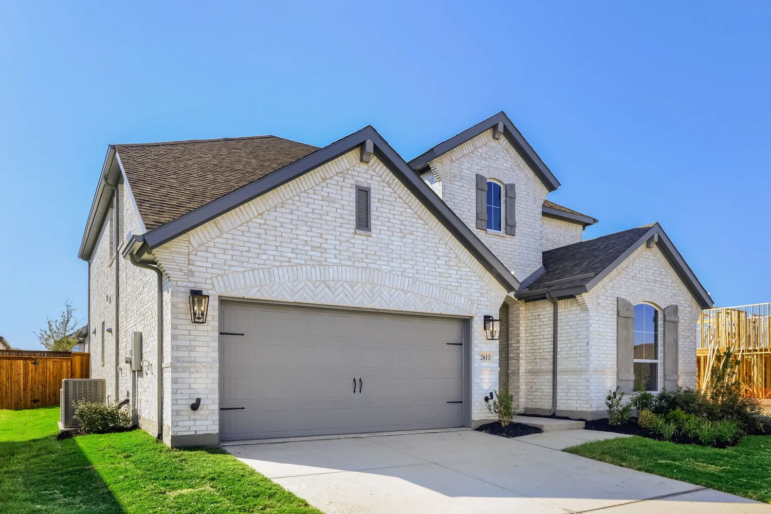 White brick exterior with gray trim, attached garage, arched window accents, and a landscaped front yard