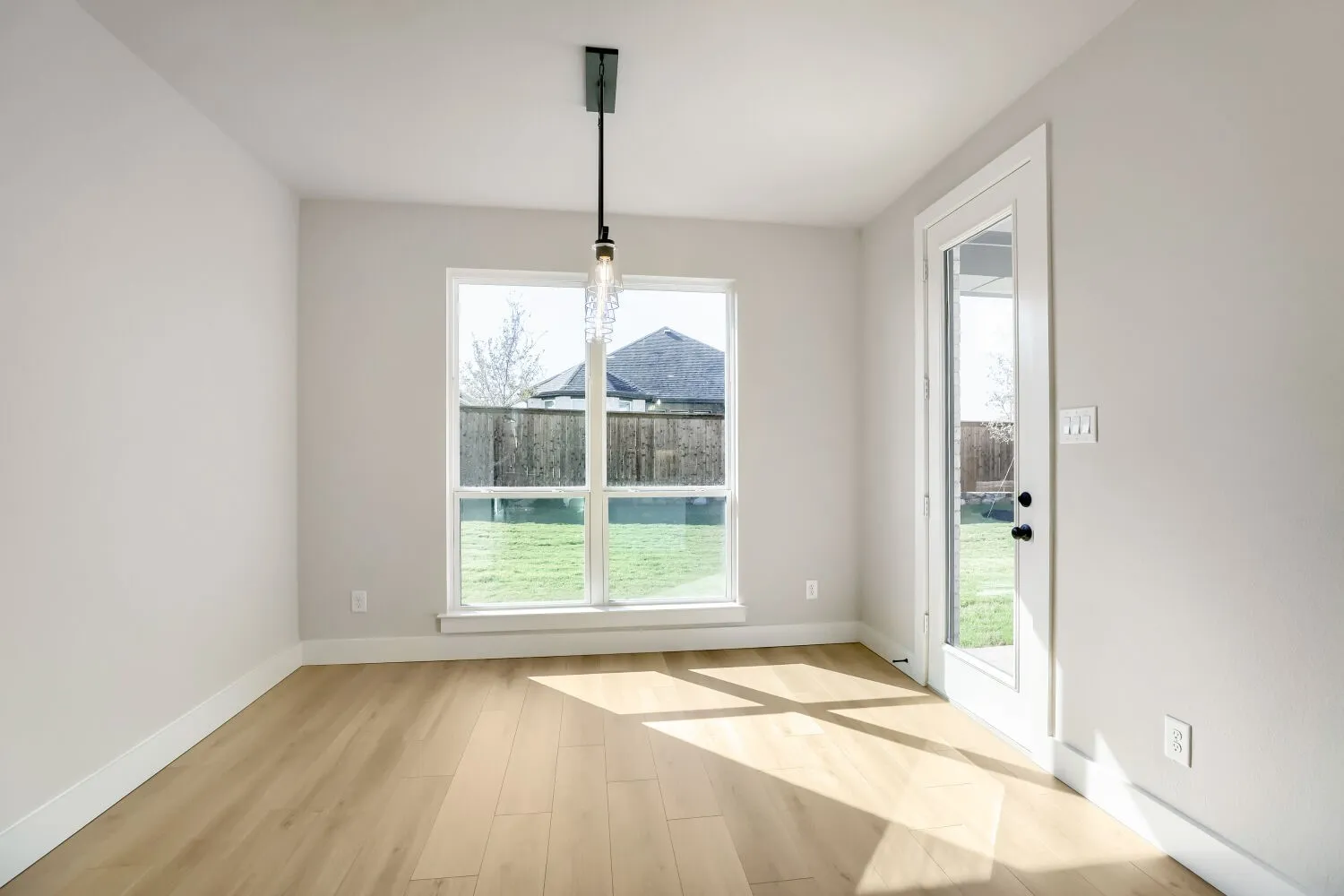 Light-toned wood-finish flooring, white walls, and a contemporary pendant light fixture
