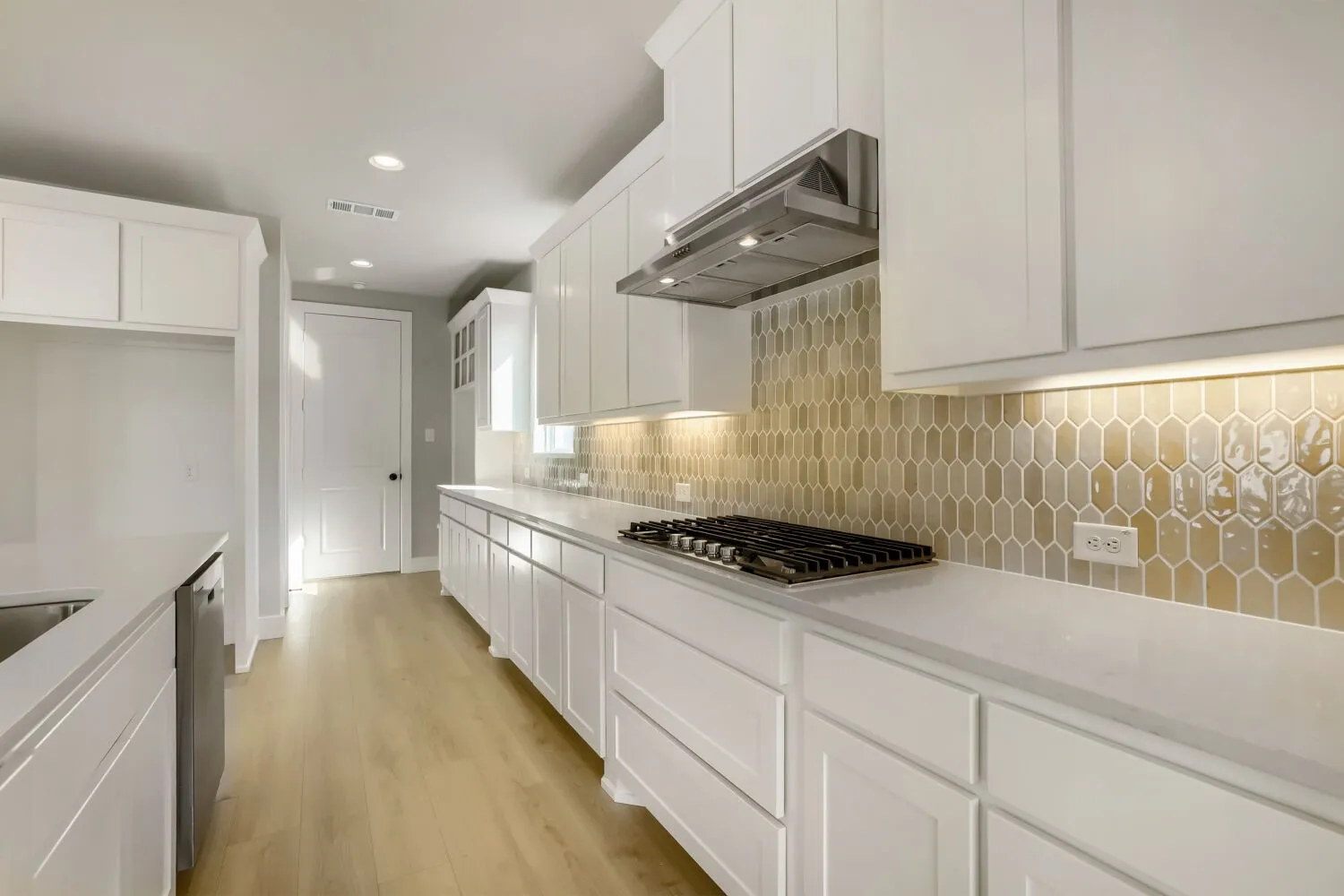 Kitchen featuring white shaker-style cabinetry, light-toned wood-finish flooring, a built-in gas range, stainless steel range hood, and a picket tile backsplash