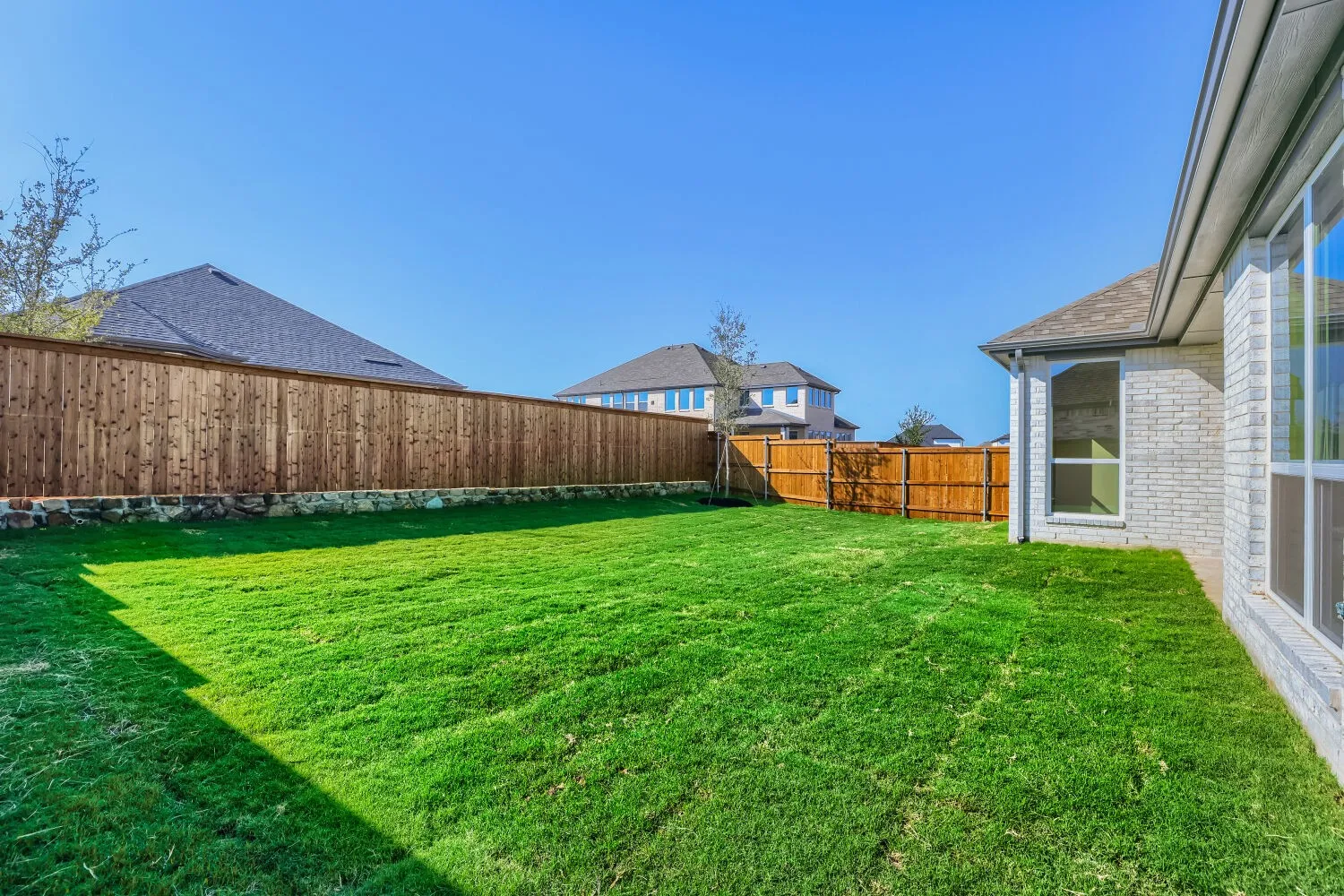 Expansive grassy yard with a wood privacy fence and stone base