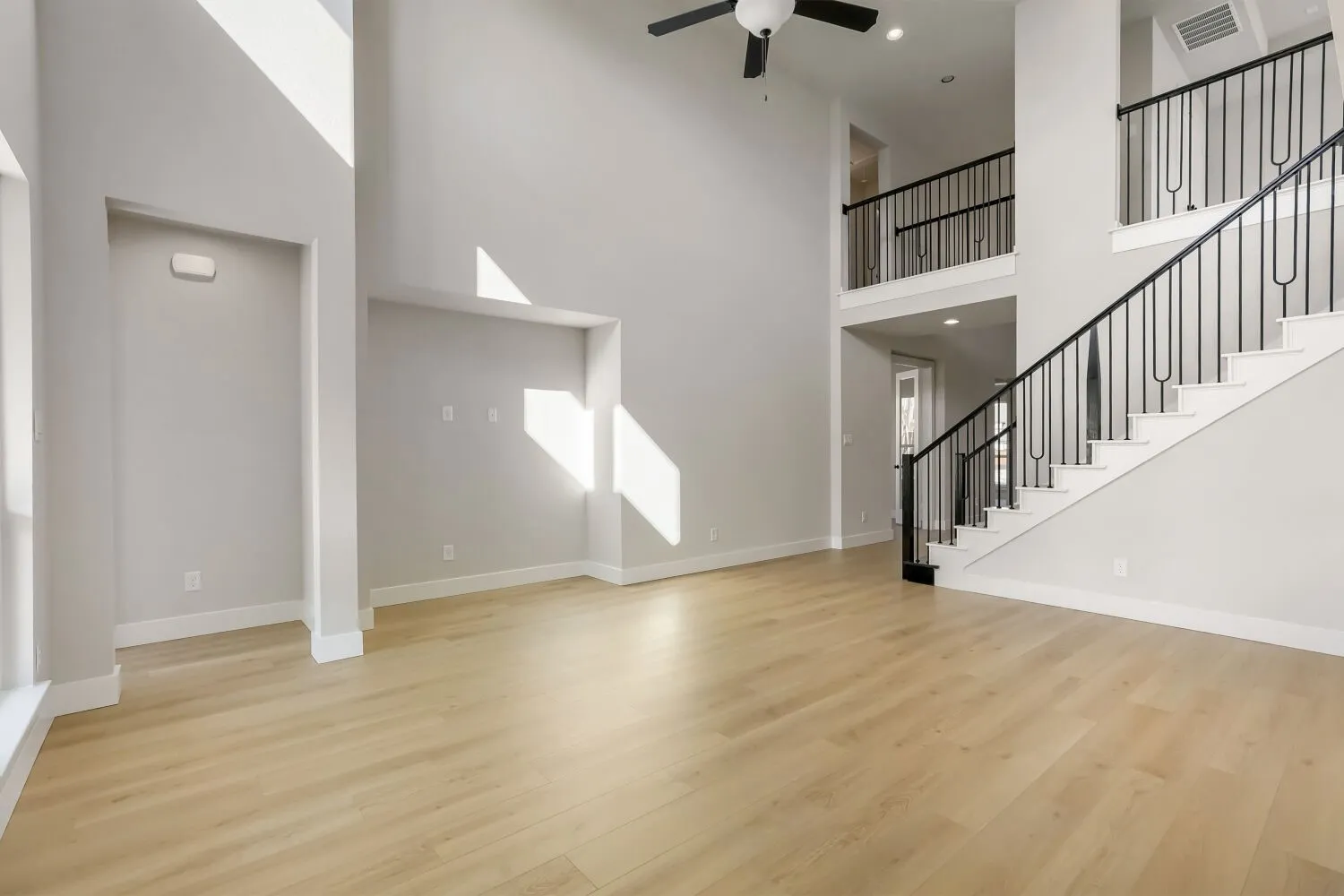 Two-story ceiling, wood-finish flooring, built-in niches, and a staircase with decorative metal balusters