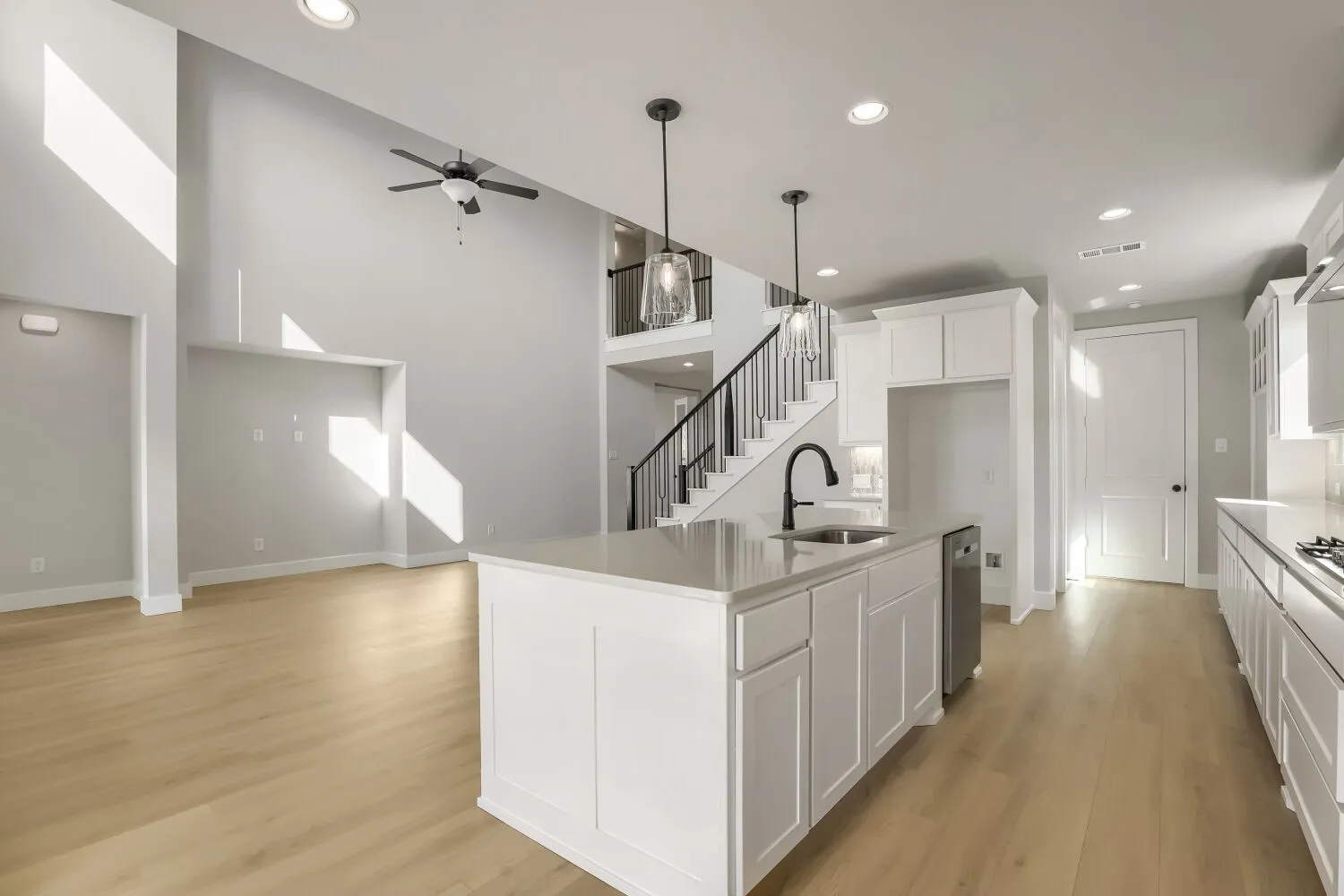 Kitchen island with an undermount sink and gooseneck faucet, light wood-finish flooring, two-story ceiling, recessed lighting, and white cabinetry