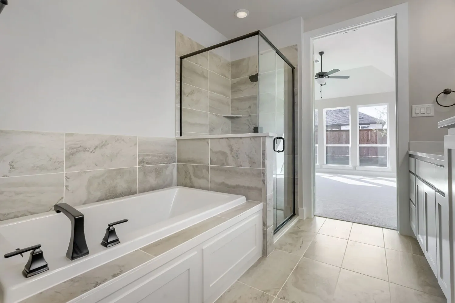 Soaking tub with black fixtures, glass-enclosed shower, tile flooring, built-in cabinetry, and neutral wall tones