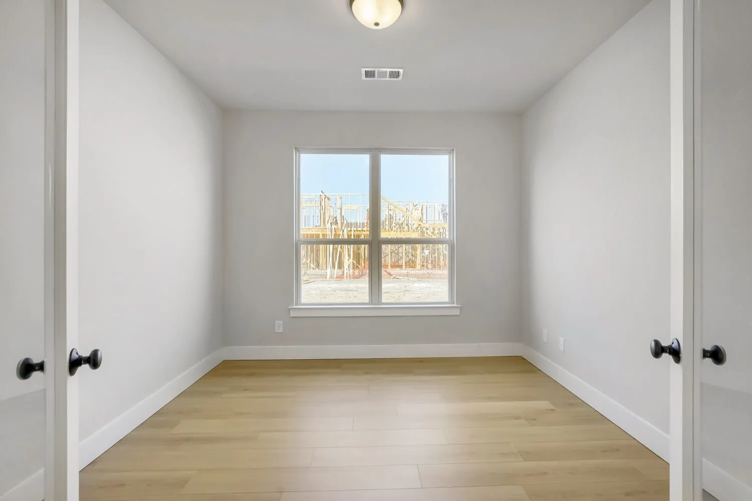 Bright, light-filled bedroom with wood-finish flooring, dual closets with black hardware, and large double-hung window framing city skyline views