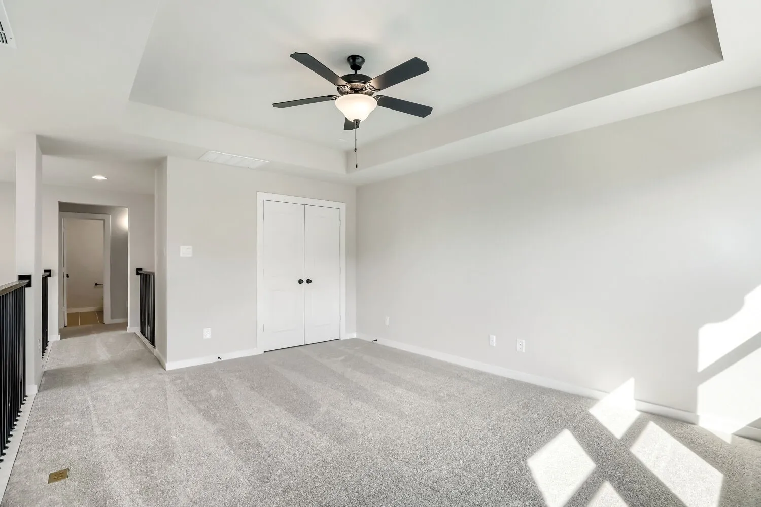 Carpeted room featuring a tray ceiling, ceiling fan with light fixture, double-door closet, and painted walls