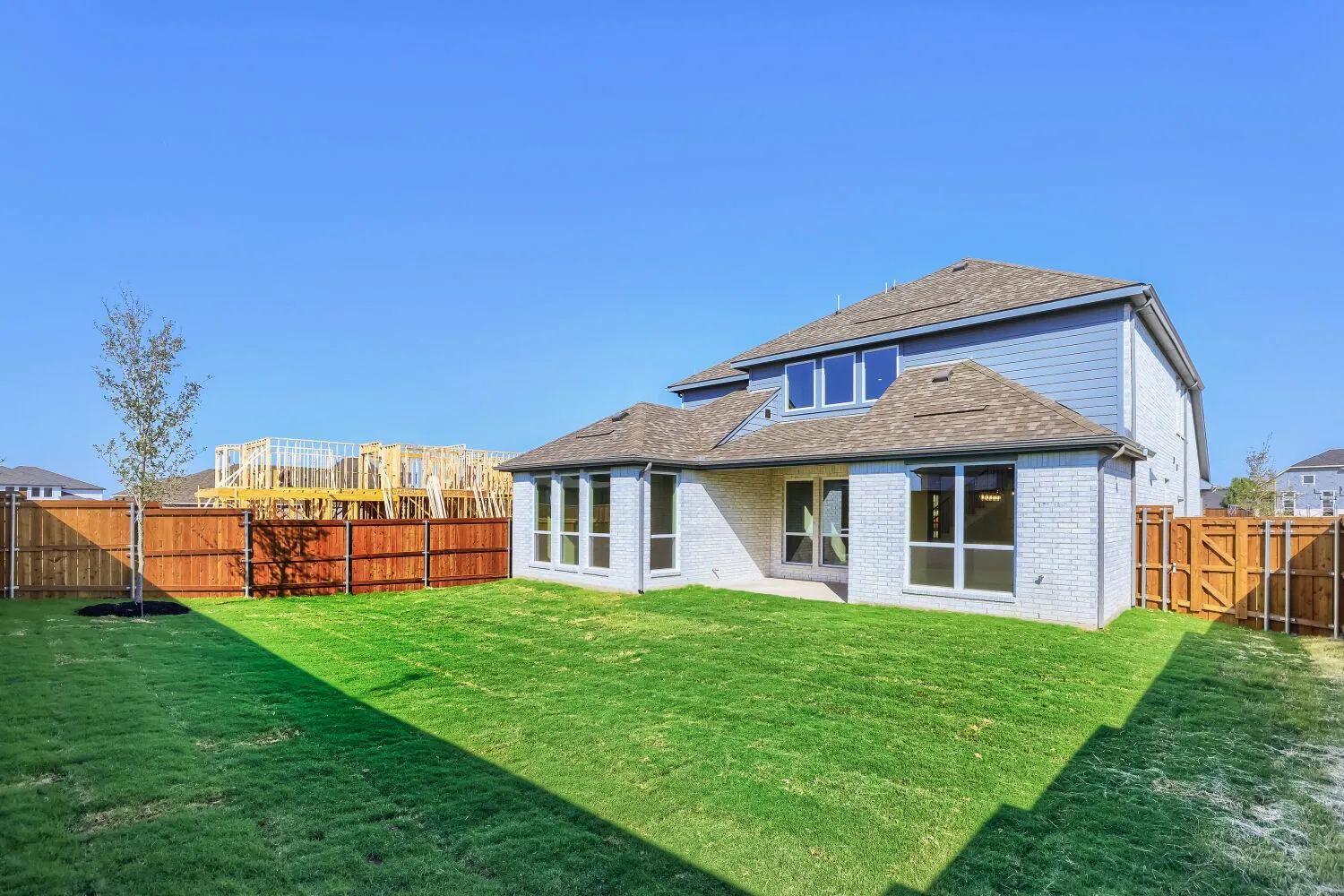 Expansive green lawn, light brick exterior, privacy fencing, multiple windows, and a paved patio area