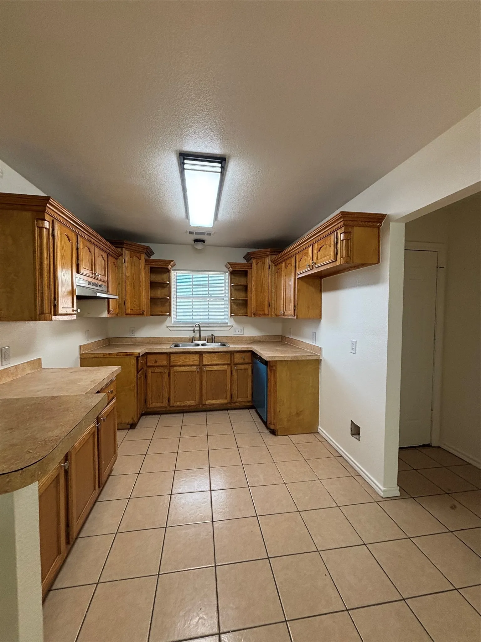 Kitchen featuring extensive wood cabinetry, L-shaped countertops, stainless steel sink, and tile flooring