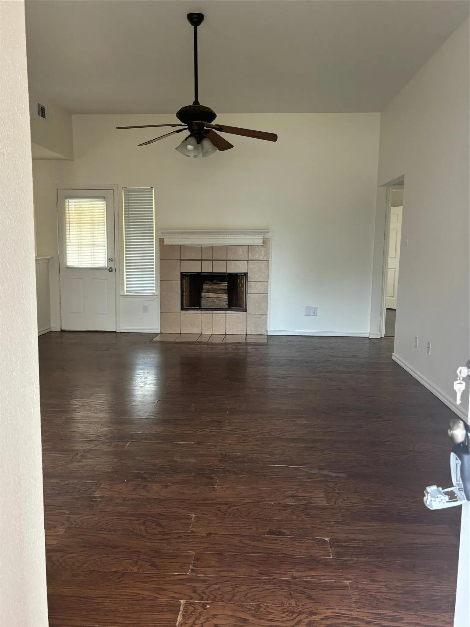 Spacious room featuring wood-finish flooring, a tile fireplace, and a ceiling fan with integrated lighting