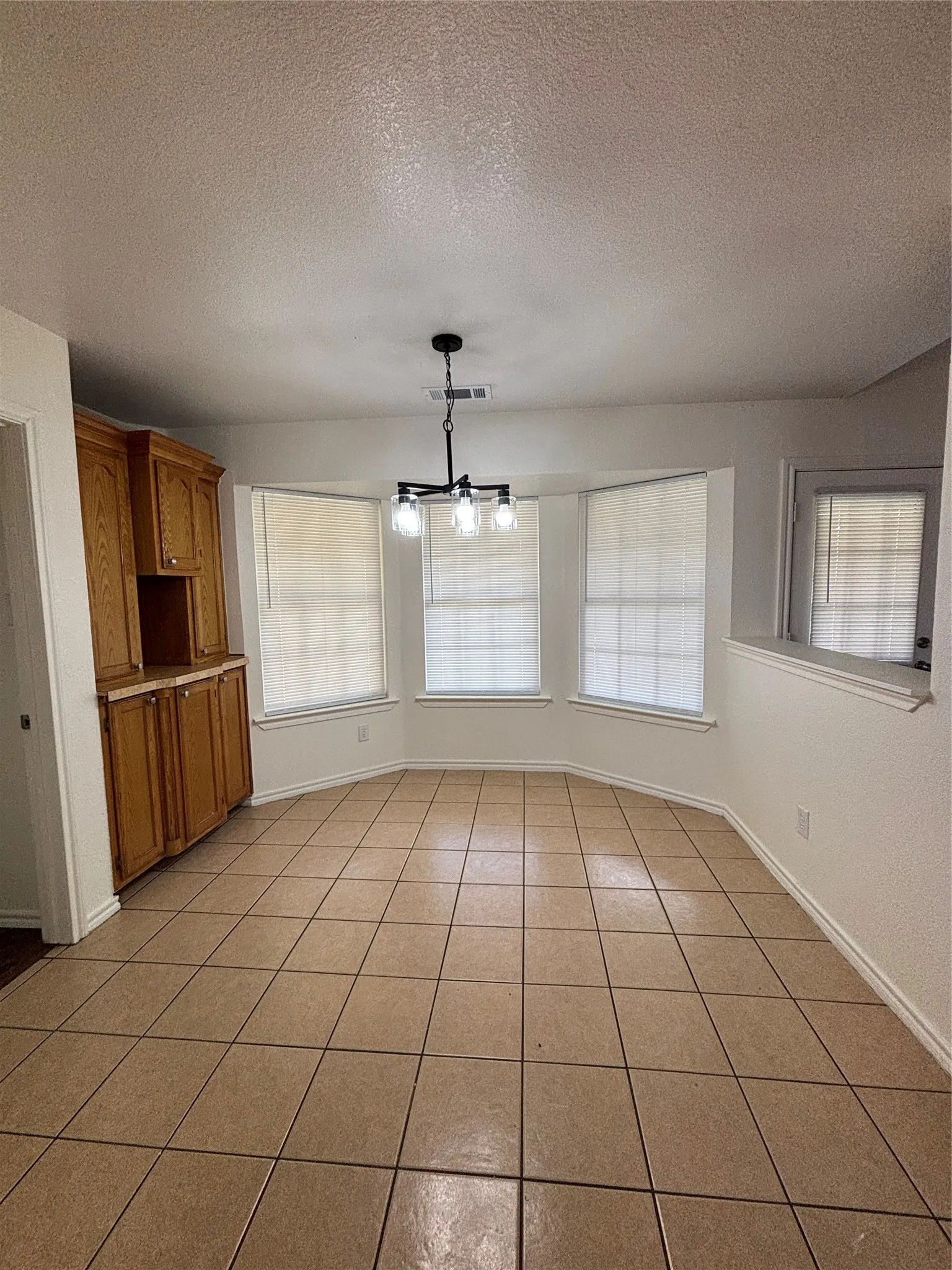 Dining area featuring a bay window with three windows, a black three-light chandelier, a built-in wood-finish cabinet, and large square tile flooring