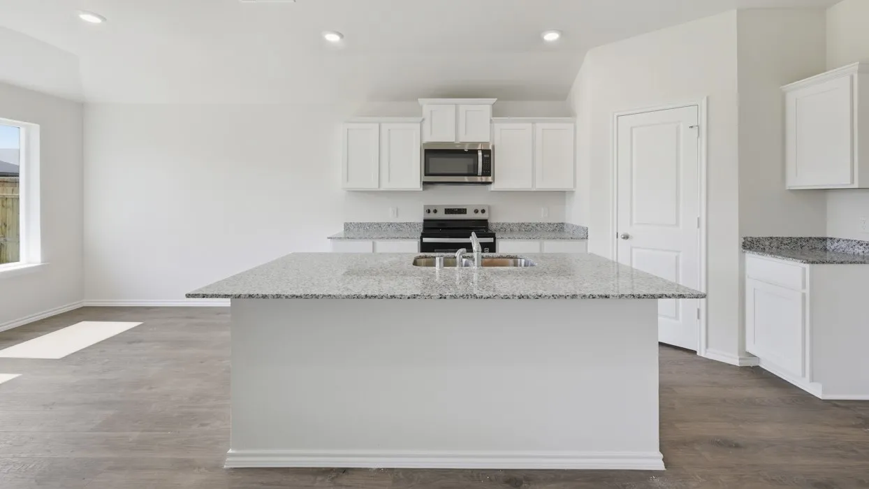 Spacious kitchen featuring a central island with an undermount sink, granite countertops, white cabinetry, stainless steel microwave, and wood-finish flooring
