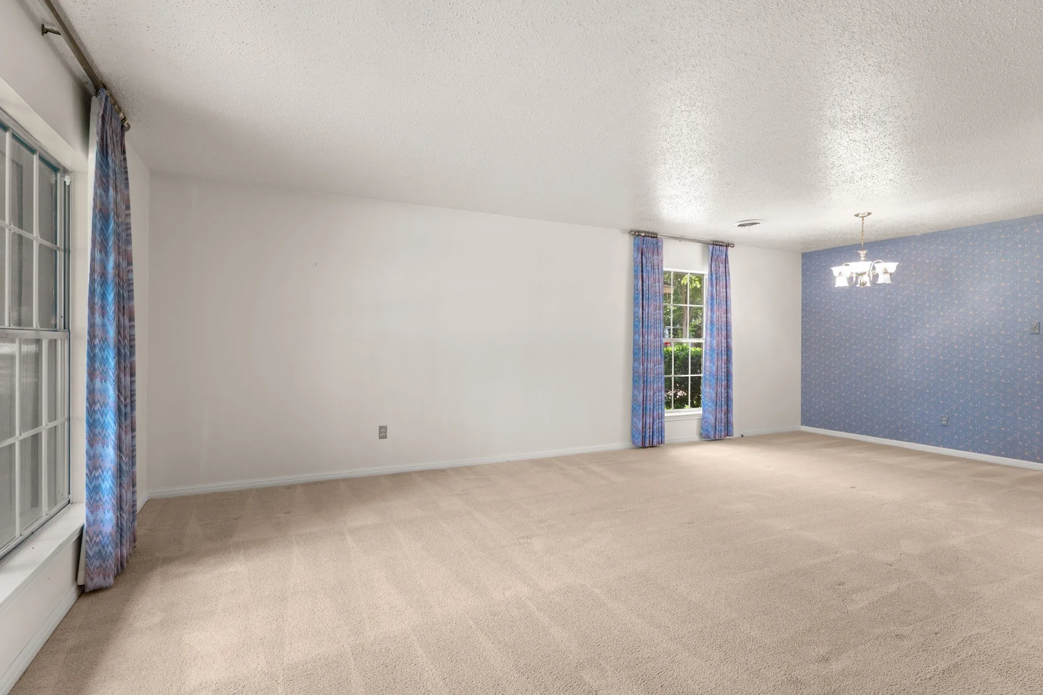 Spacious interior room with neutral carpeting, white walls, and a textured ceiling