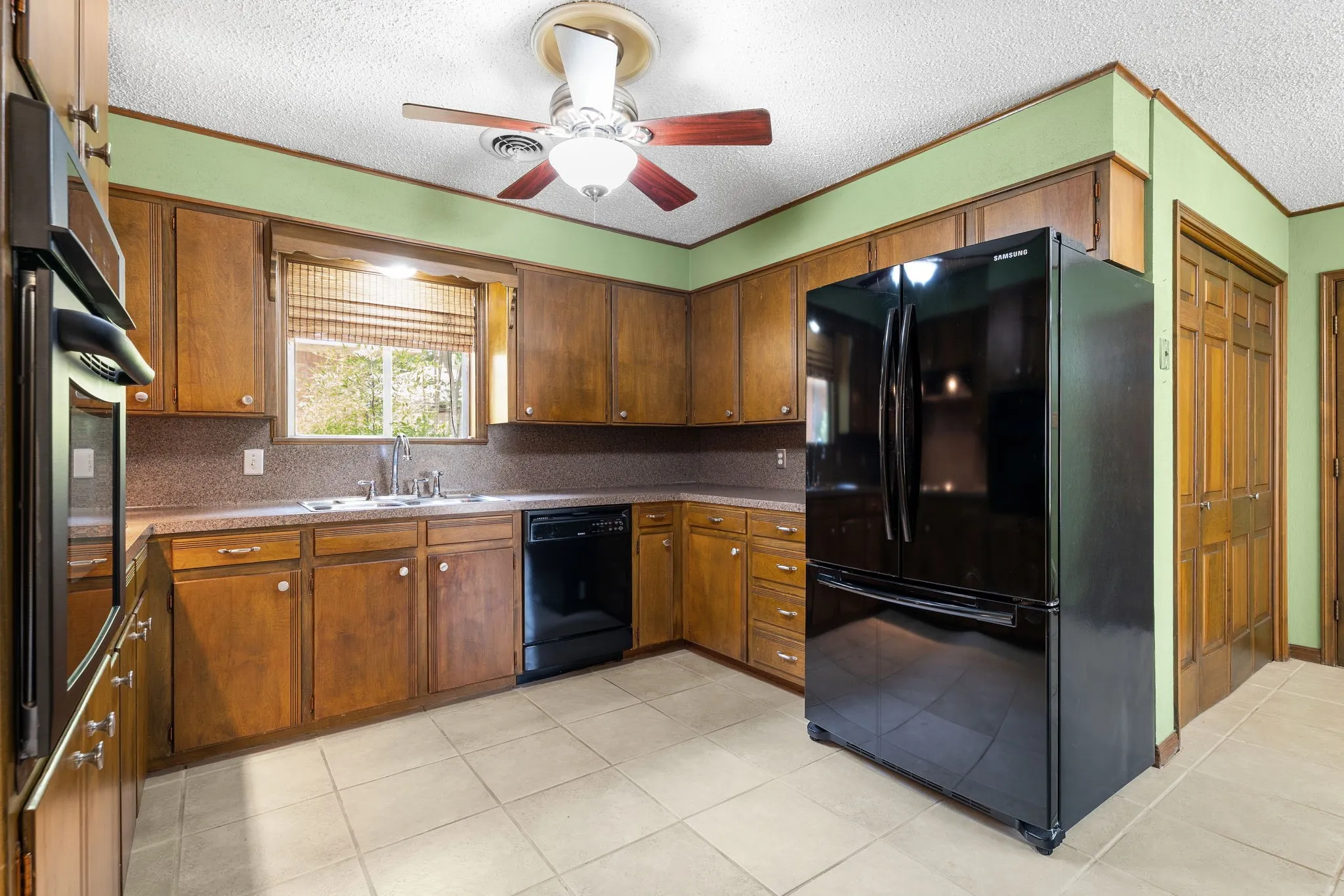 Kitchen featuring wood cabinetry, integrated black appliances, a ceiling fan, a window over the sink, and tile flooring