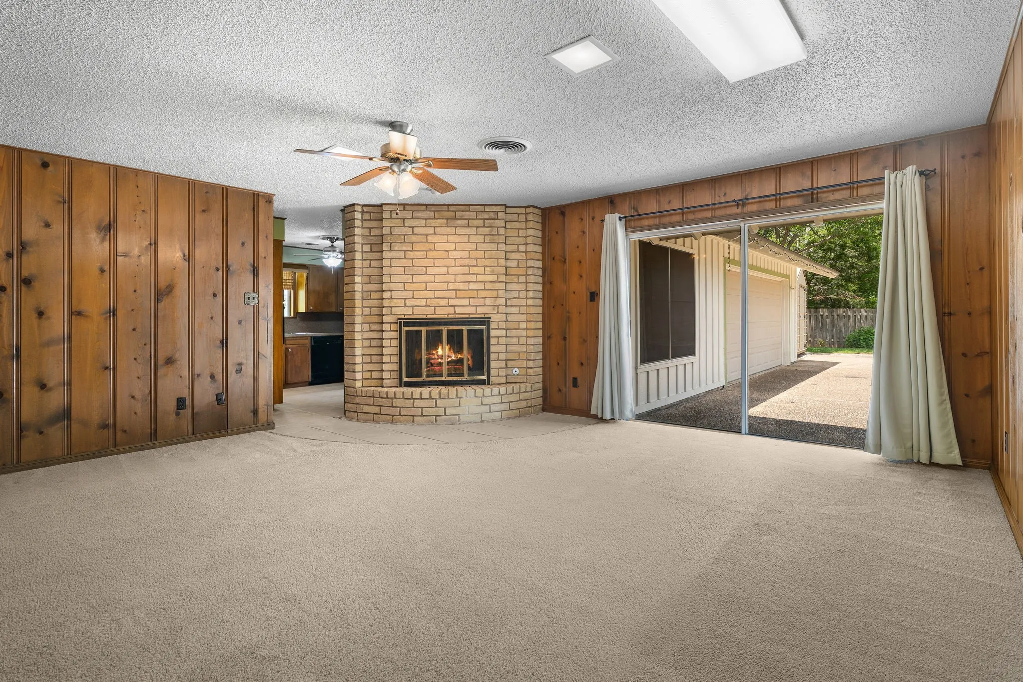 Living area featuring wood paneling, a brick fireplace, and light-toned carpeting