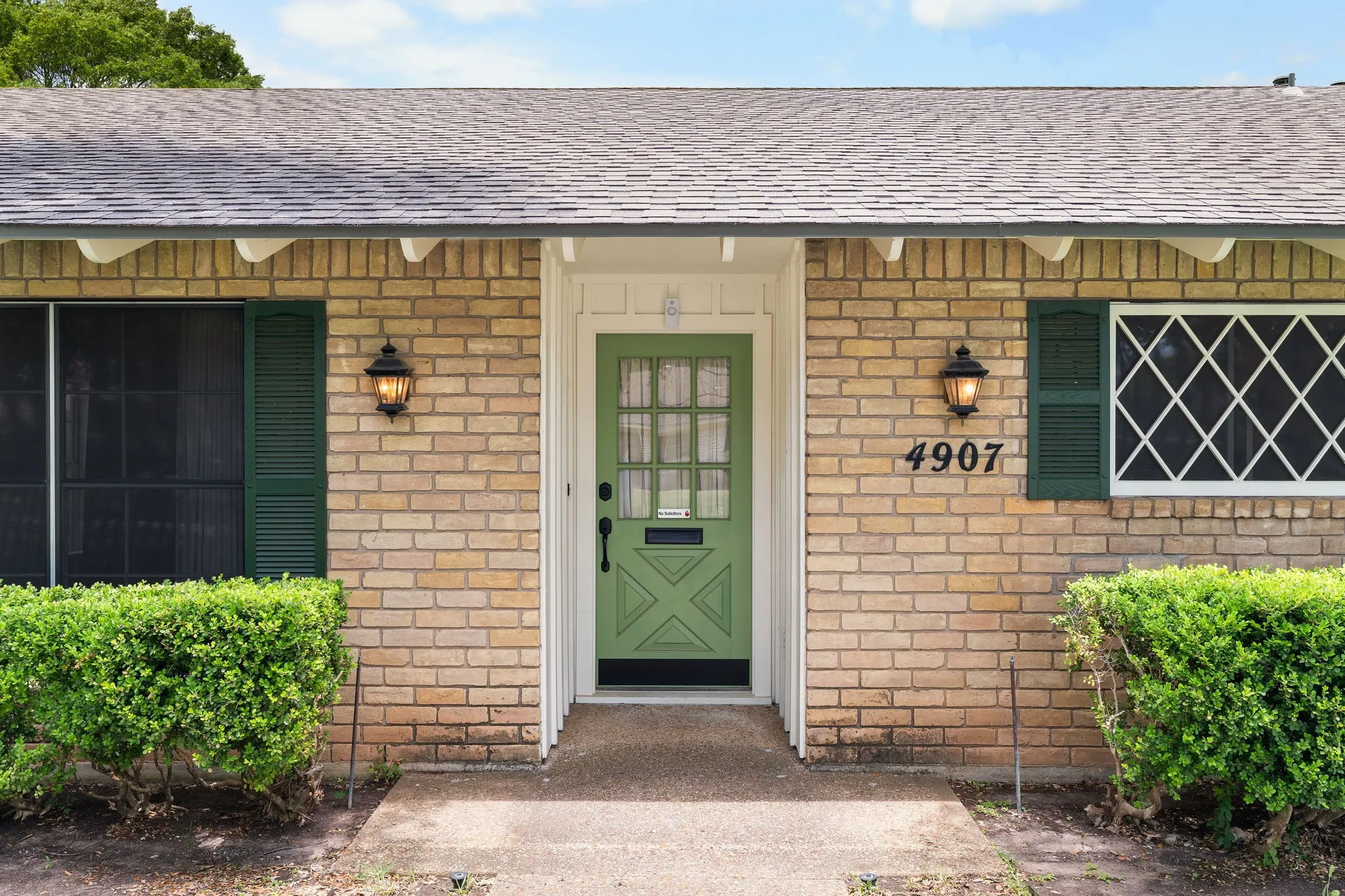 Brick exterior featuring a green paneled door with black hardware, flanked by two outdoor wall lanterns