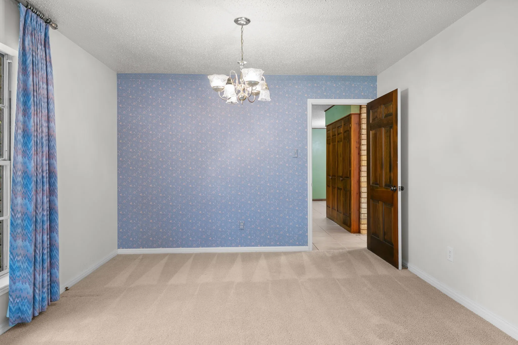 Spacious room featuring patterned blue wallpaper, a polished chrome chandelier, and light-toned carpet flooring