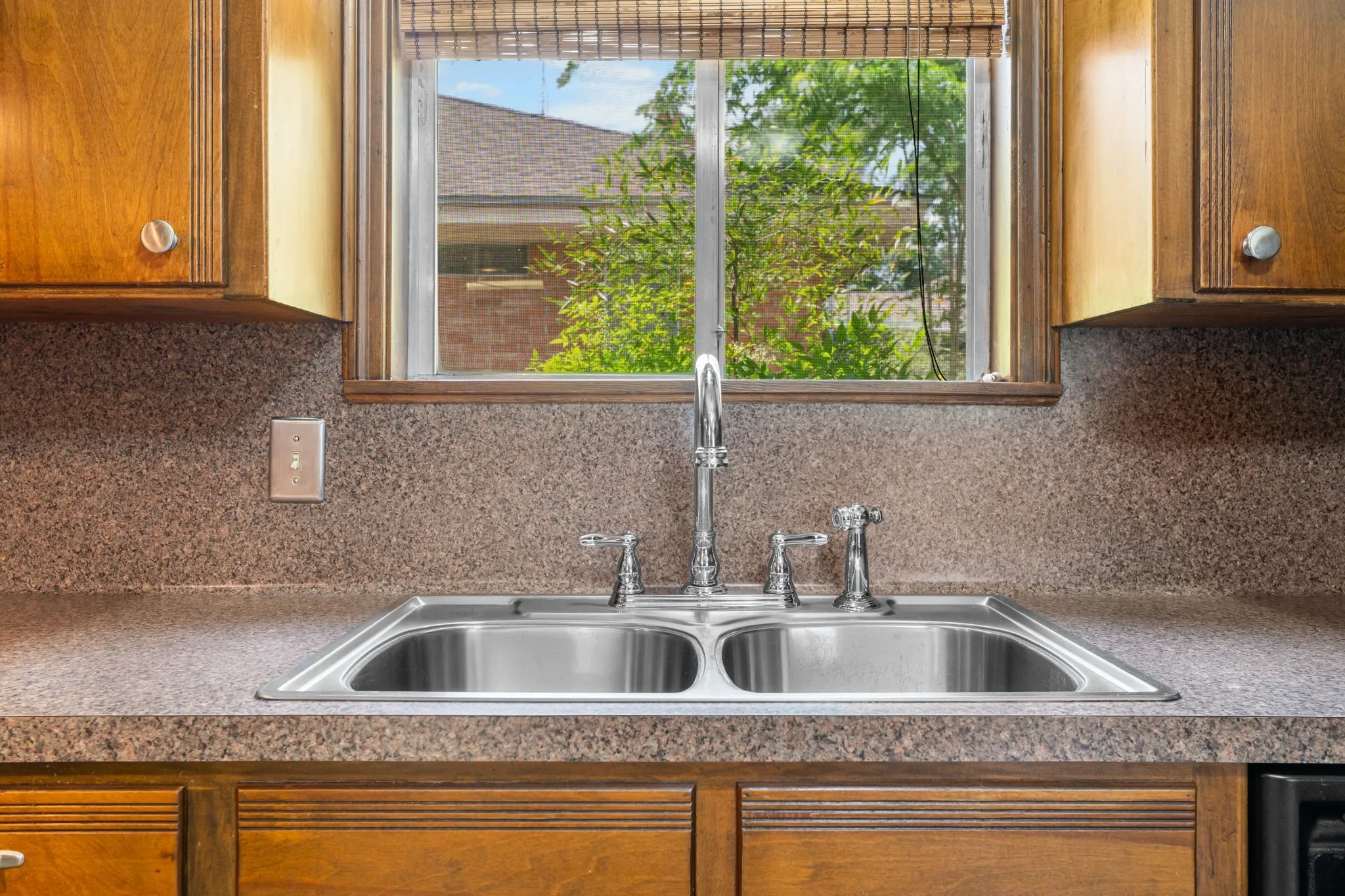 Kitchen area featuring a double basin stainless steel sink with a chrome faucet, speckled countertop, and wood cabinetry