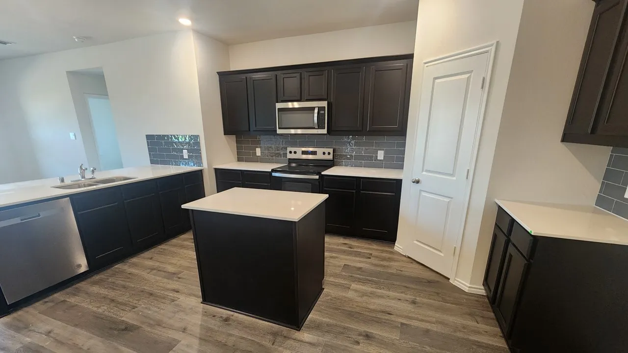 Modern kitchen featuring dark wood-finish cabinetry, light stone-finish countertops, and a subway tile backsplash