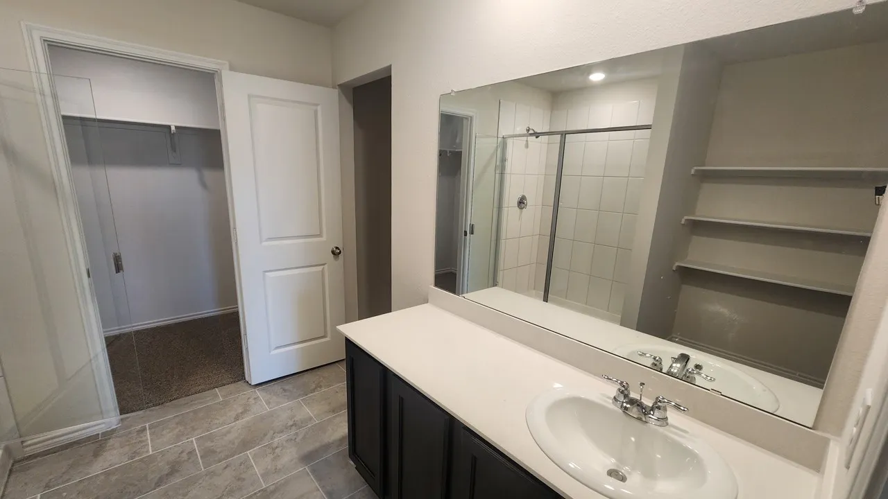 Bathroom vanity featuring a single basin sink, chrome faucet, and expansive wall-mounted mirror