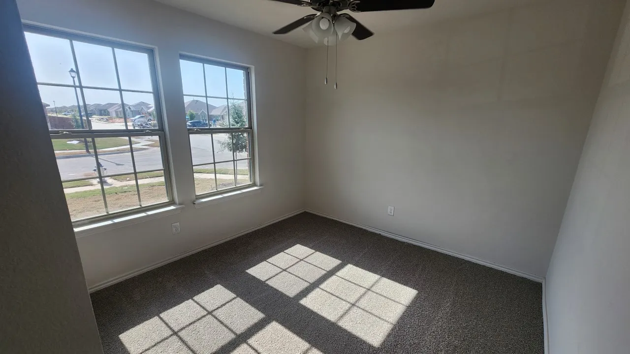 Room featuring two large windows, neutral-toned carpeting, and a ceiling fan with integrated lighting