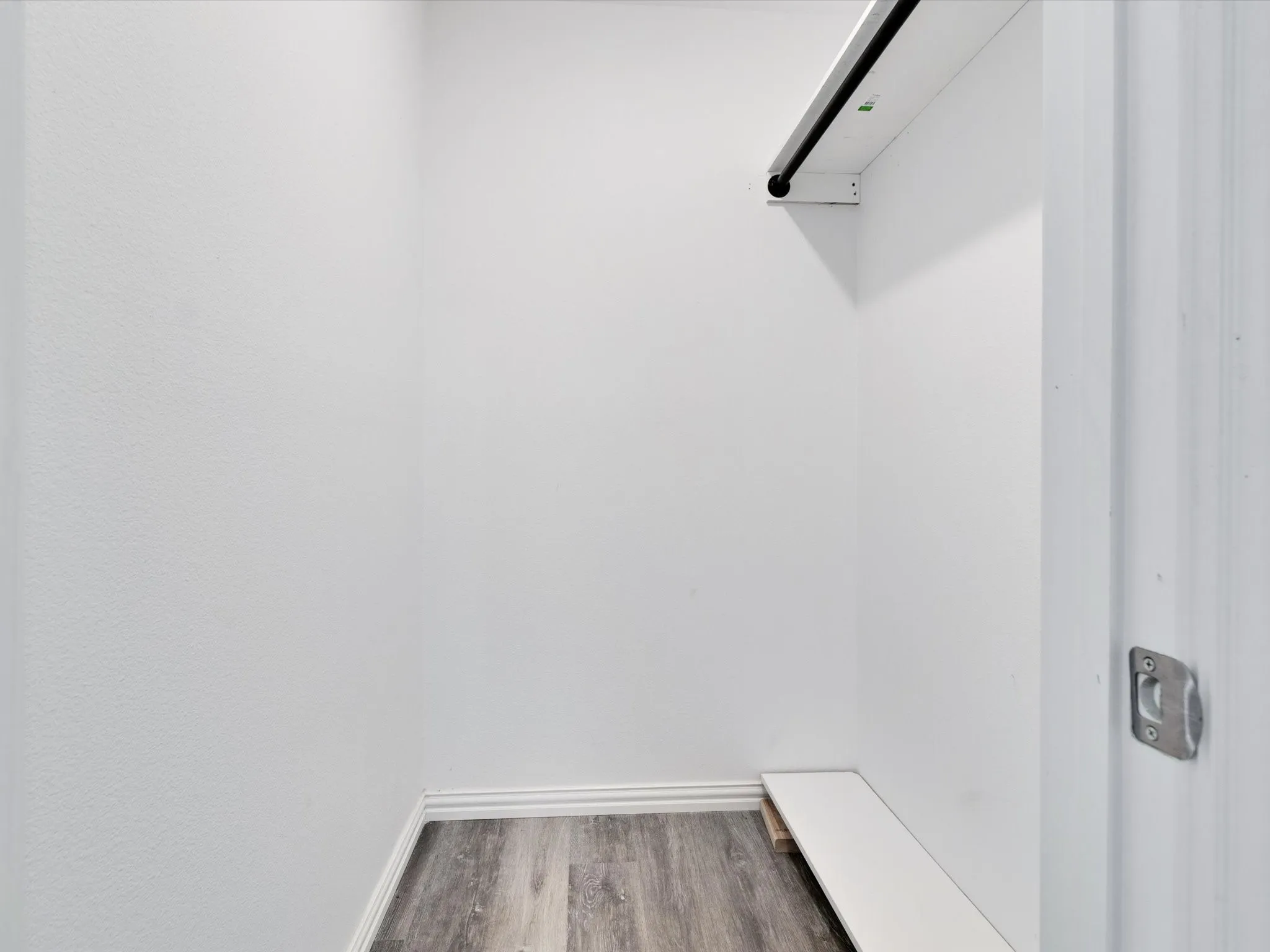 Reach-in closet featuring a hanging rod, integrated shelving, wood-finish flooring, and crisp white walls