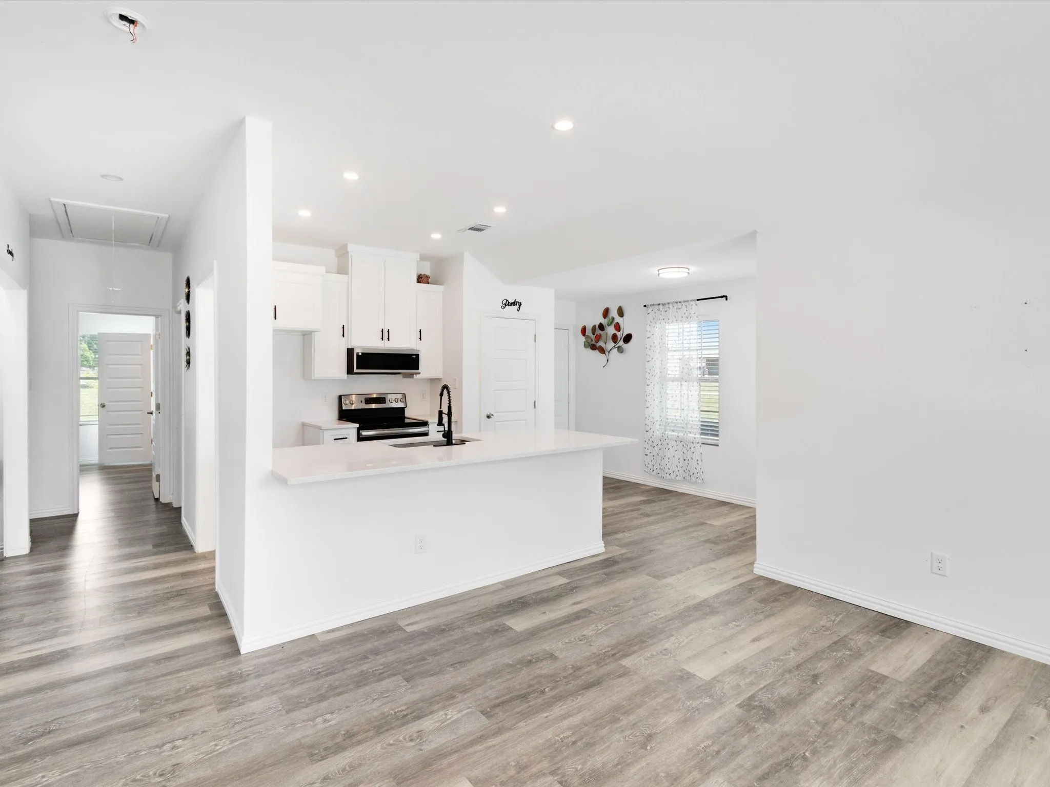 Open-concept kitchen and living area featuring wood-finish flooring, recessed lighting, white cabinetry, a kitchen island with sink, and black appliances
