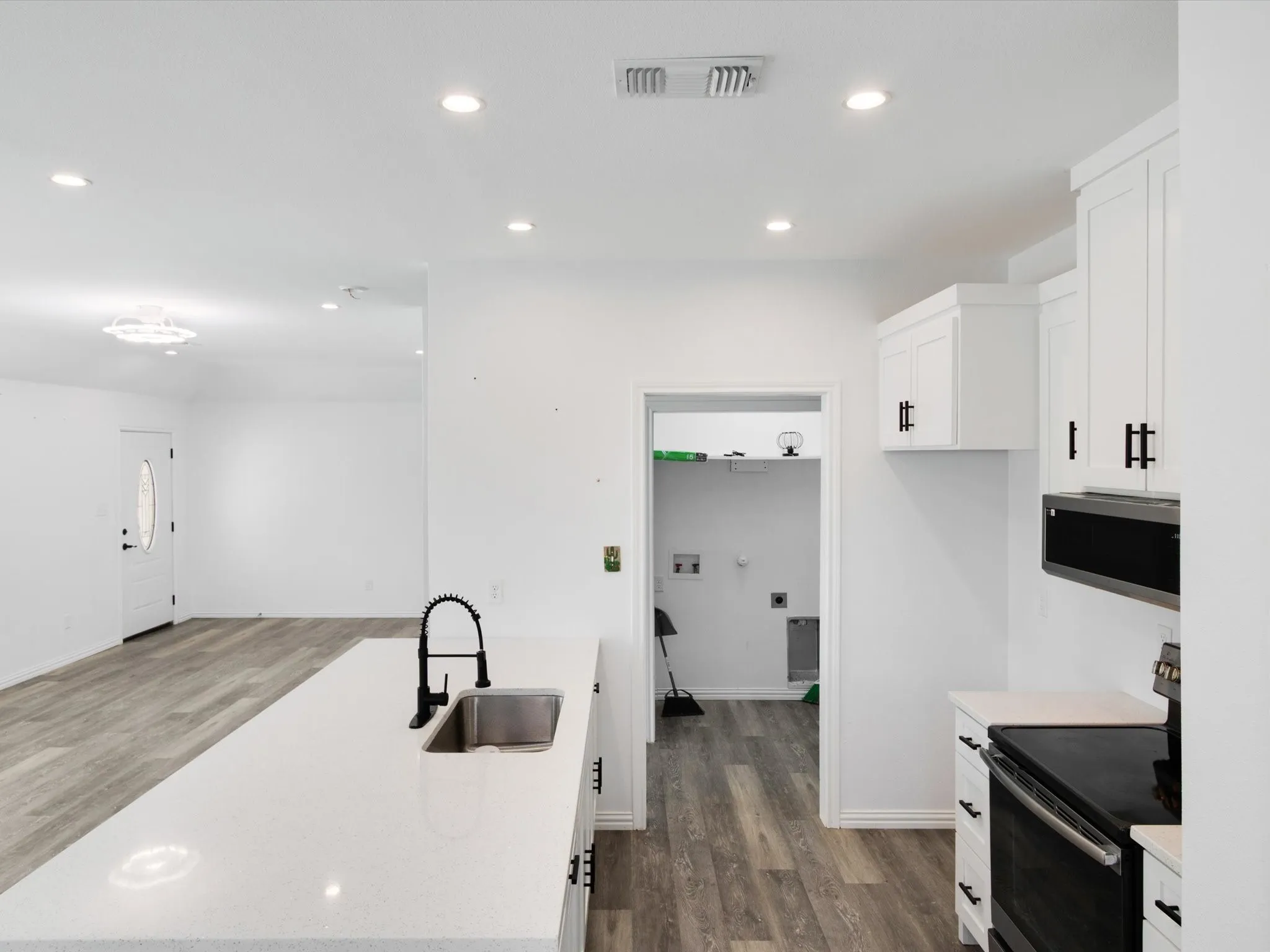 Contemporary kitchen featuring white cabinetry with black hardware, a stainless steel sink with a matte black faucet, and a white countertop island