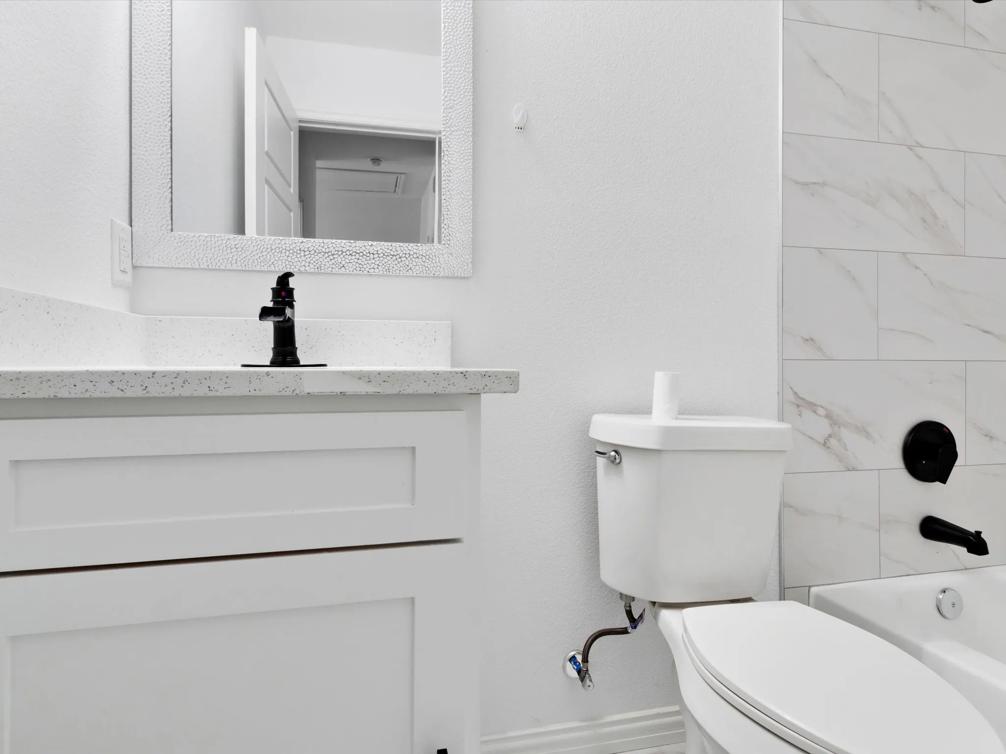 Bathroom featuring a white vanity with shaker-style cabinetry, a speckled countertop, and a black-finish faucet