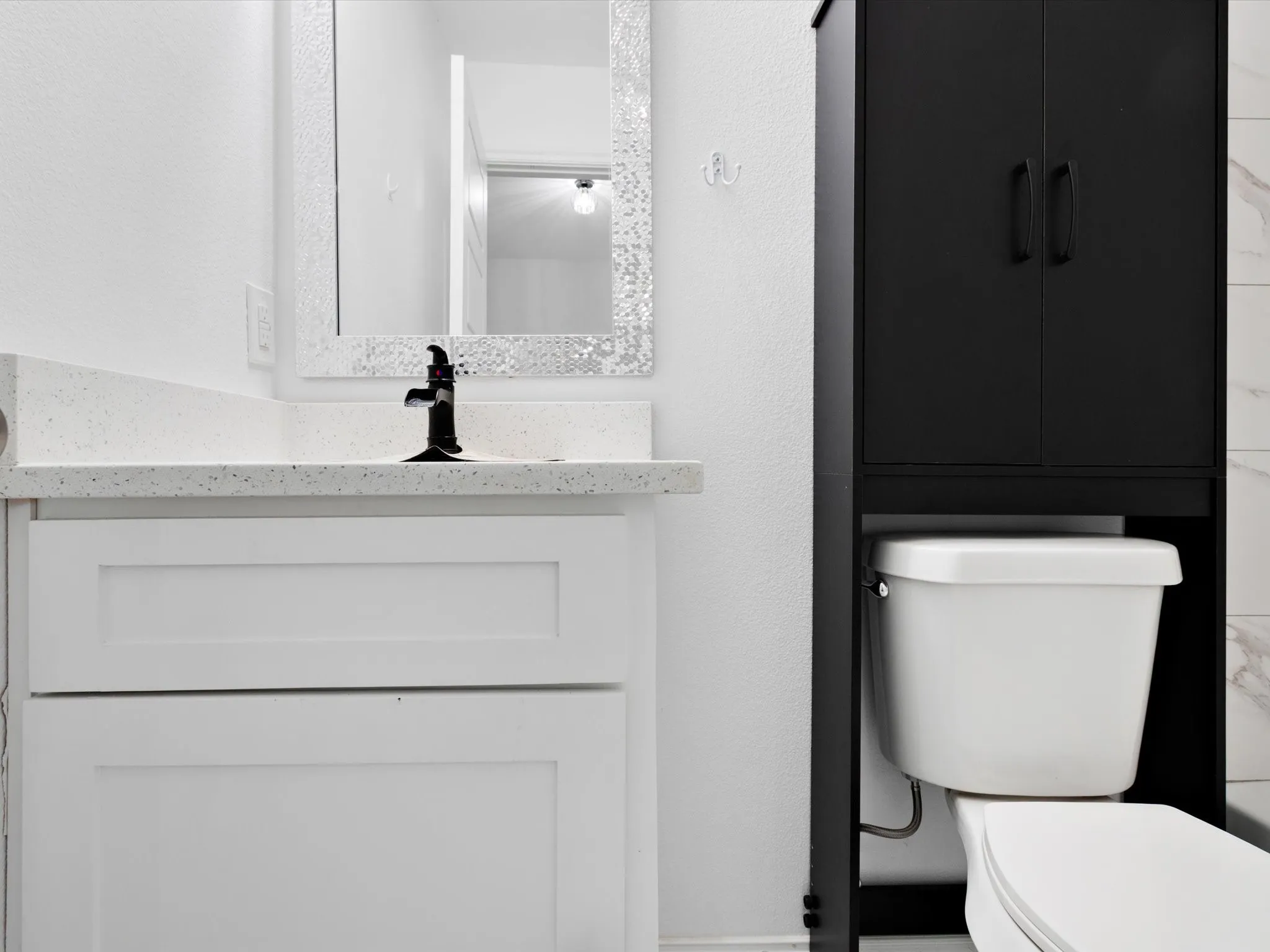 Bathroom featuring a white shaker-style vanity, black single-handle faucet, and a black over-the-toilet storage cabinet