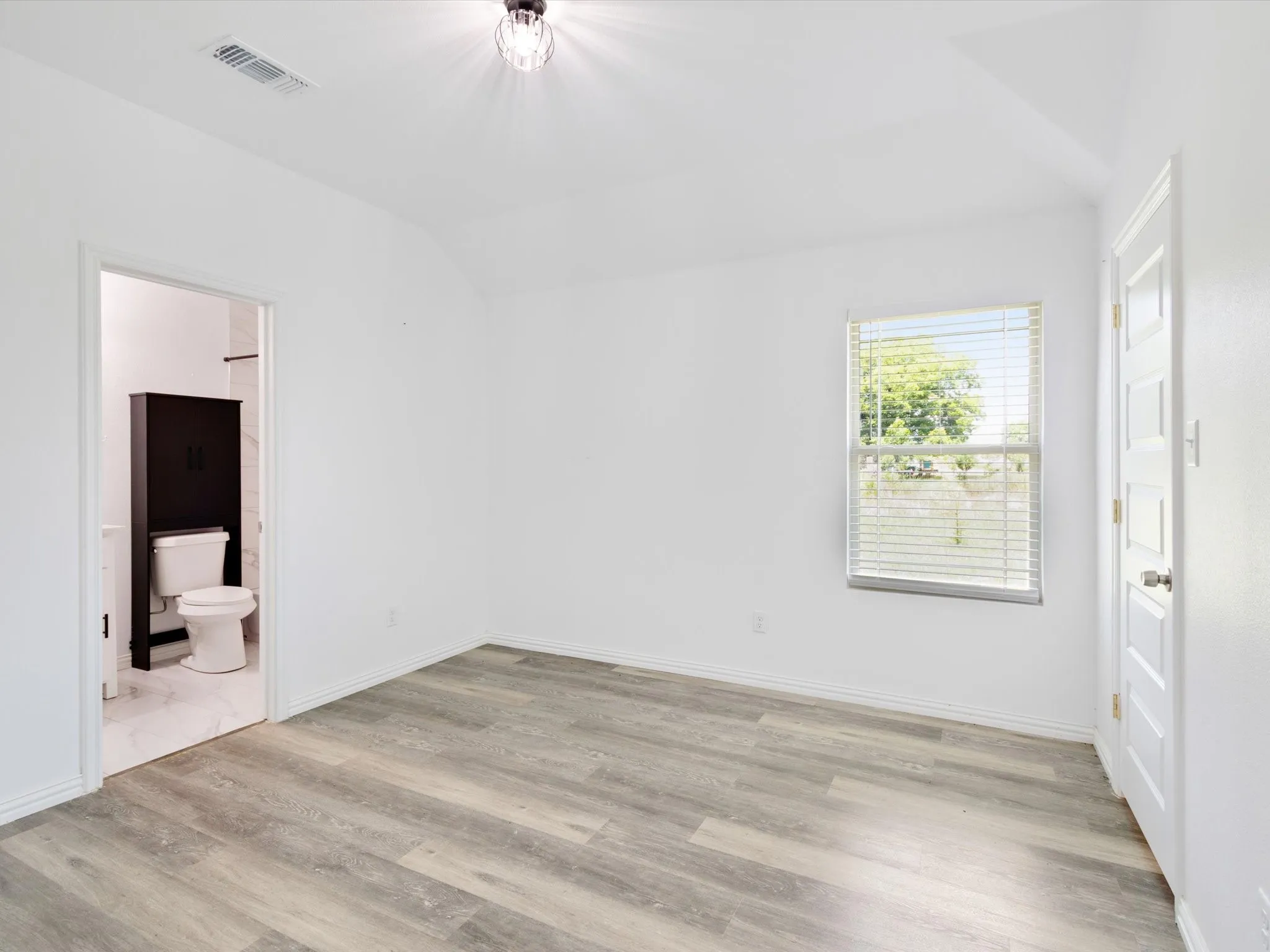 Spacious room featuring wood-finish flooring, a contemporary ceiling light fixture, and a window with horizontal blinds