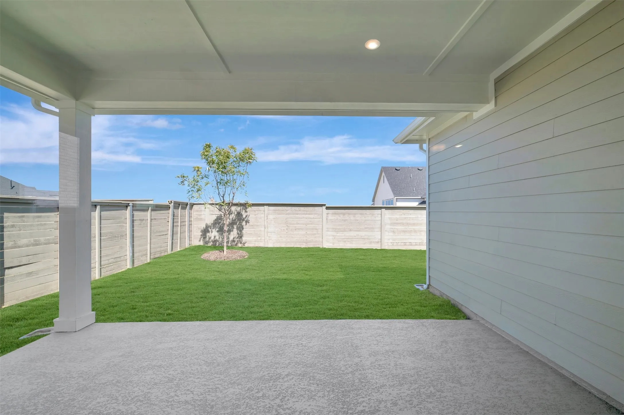 Covered patio with a textured concrete surface, recessed lighting, and a horizontal plank wall