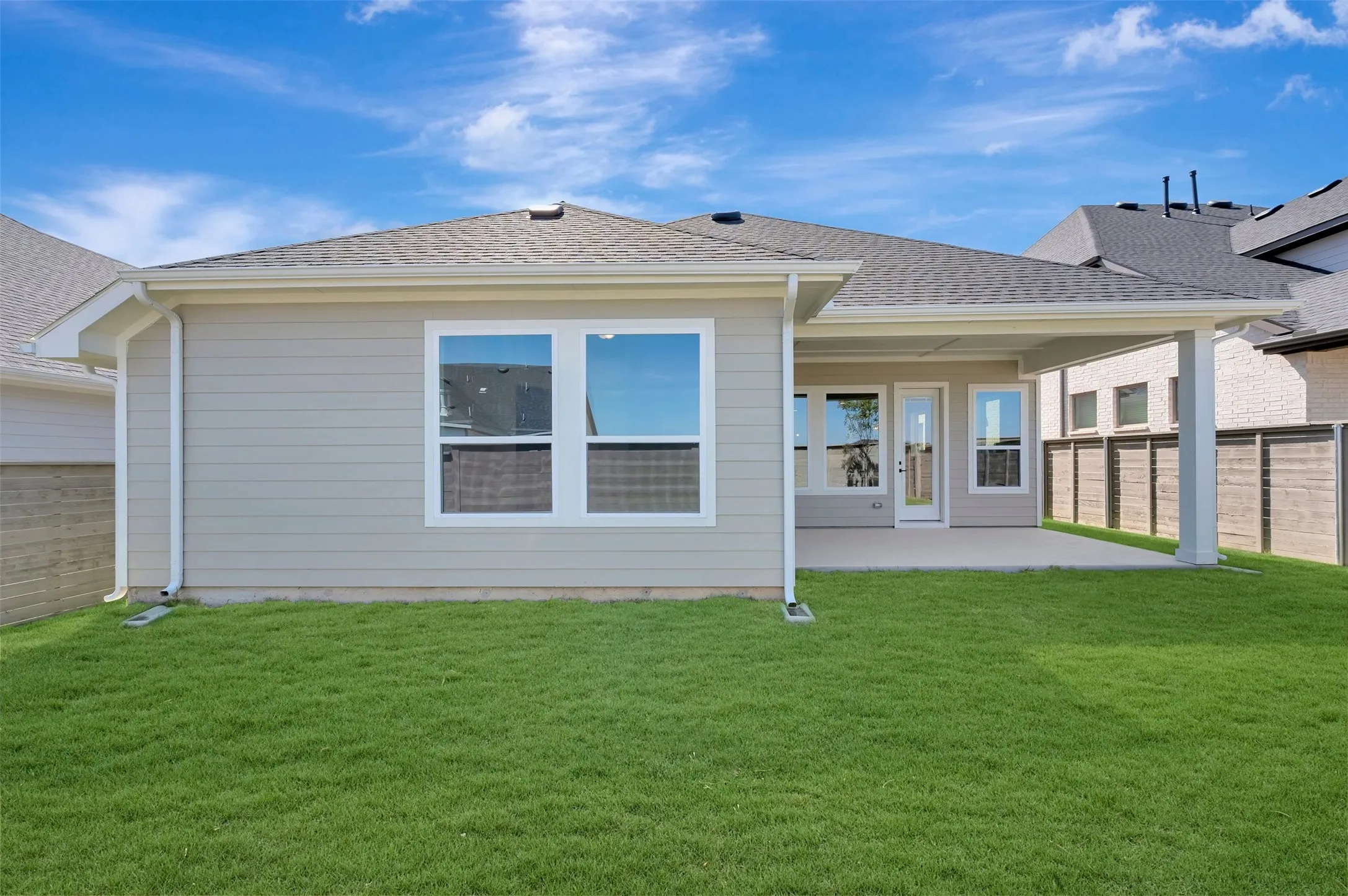 Expansive green lawn, covered patio, multiple windows, and a glass-paneled exterior door