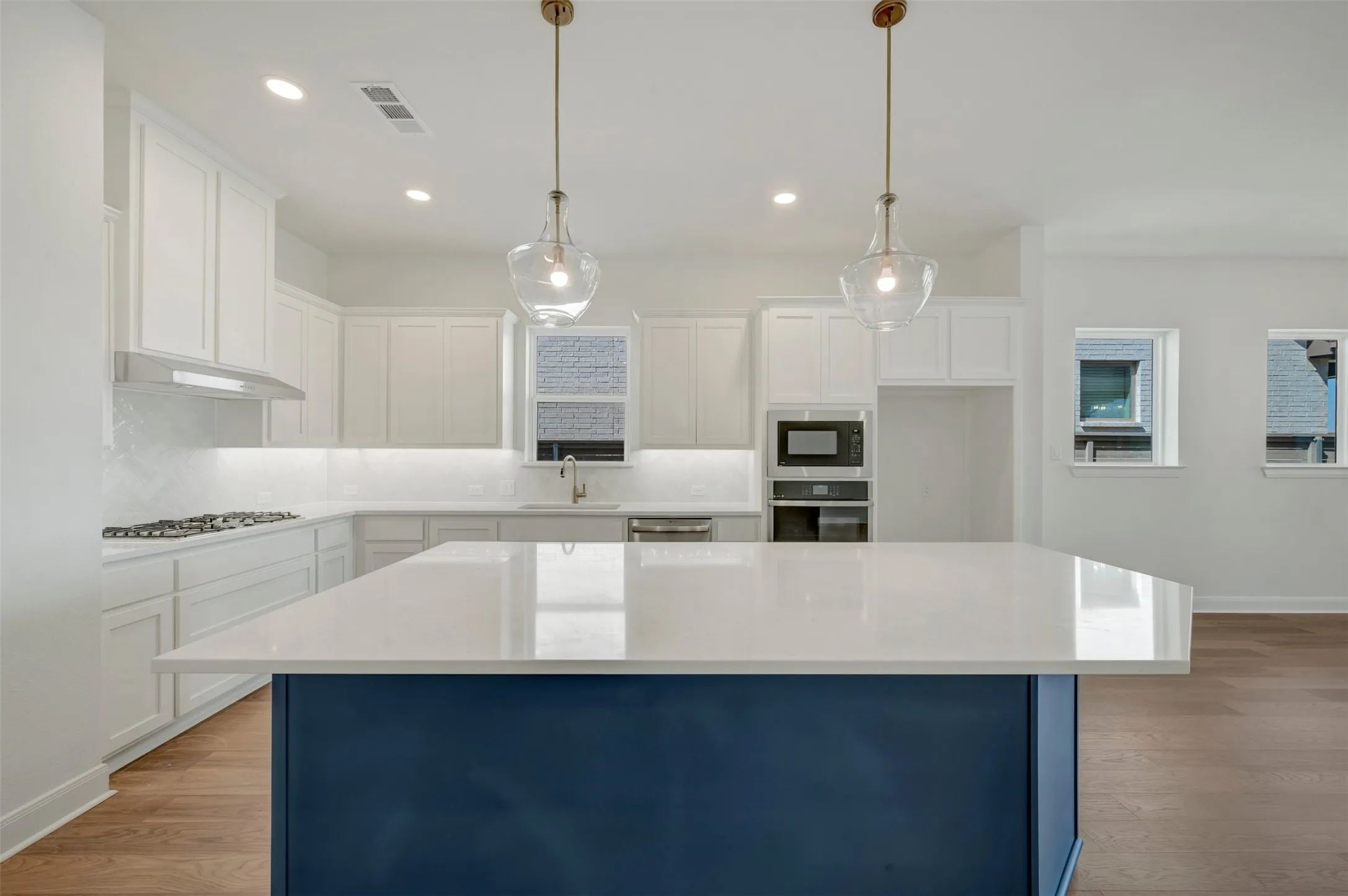 Kitchen featuring a large blue island with a white countertop, white cabinetry, a built-in microwave, and wood-finish flooring