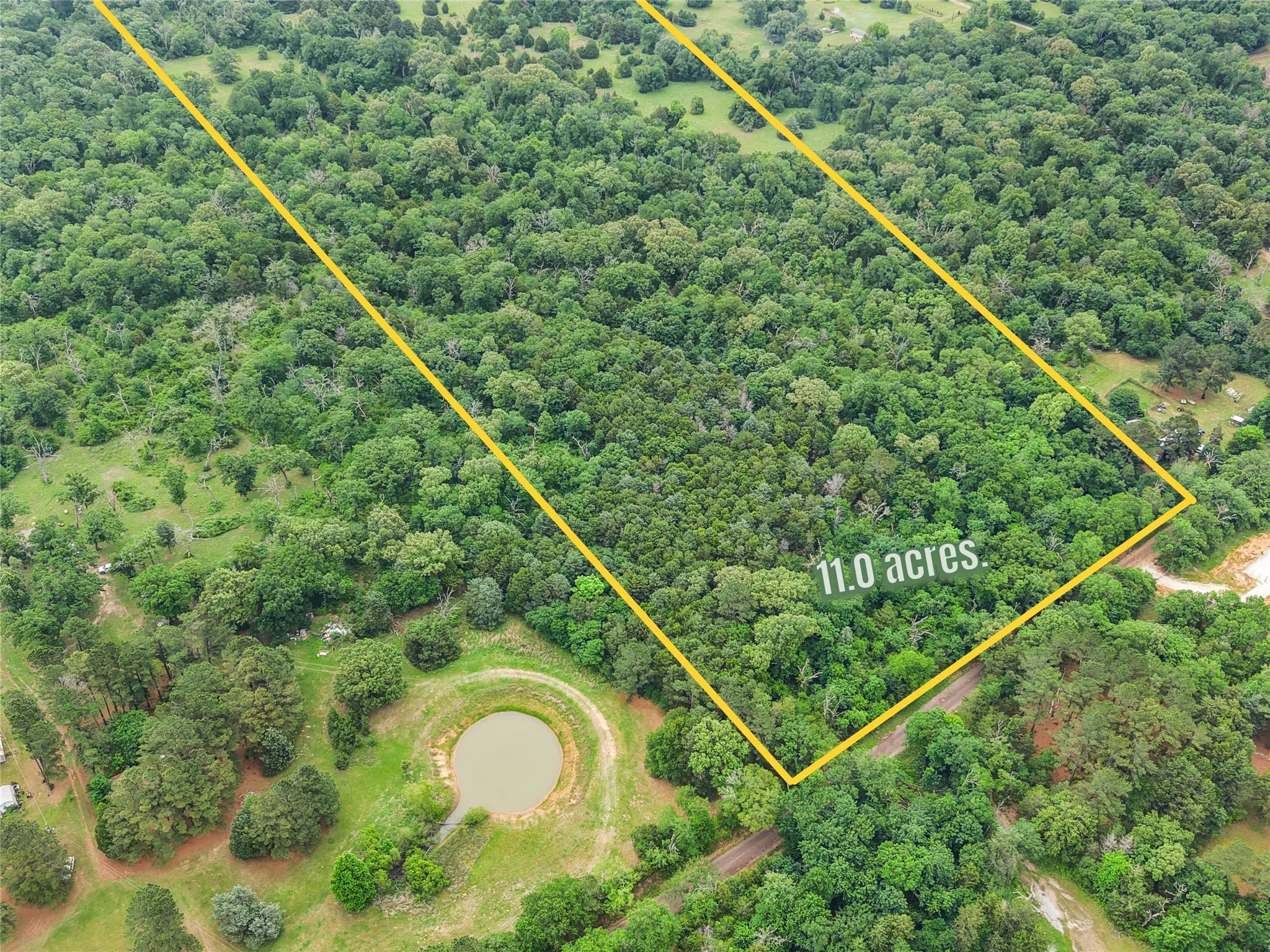 Expansive 11.0-acre property featuring dense tree coverage, a natural pond, and partial cleared areas