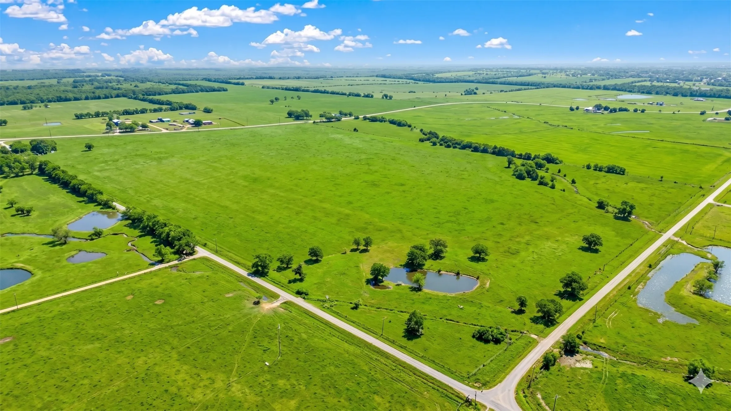 Expansive green acreage featuring multiple ponds, scattered mature trees, and unpaved roads