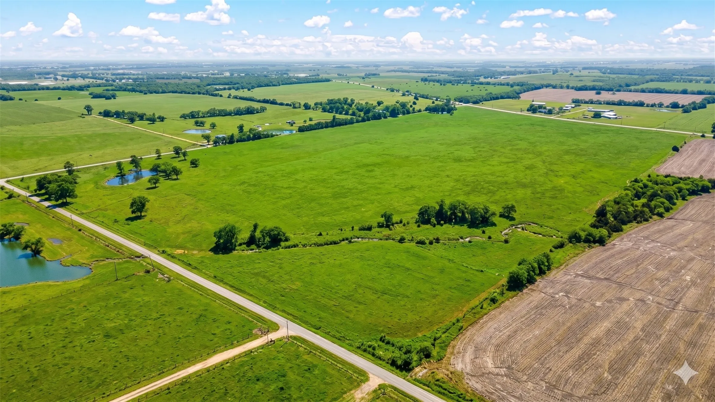 Expansive green acreage featuring multiple ponds, scattered mature trees, and a winding creek