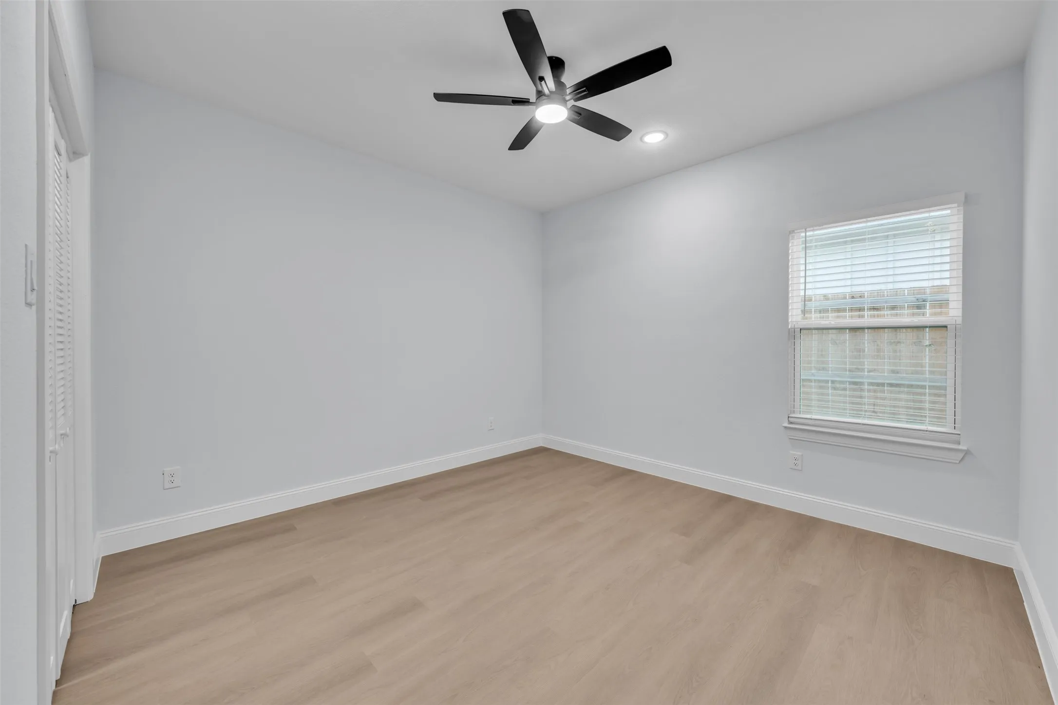 Neutral walls with white trim, wood-finish flooring, a window with blinds, and a ceiling fan with integrated lighting