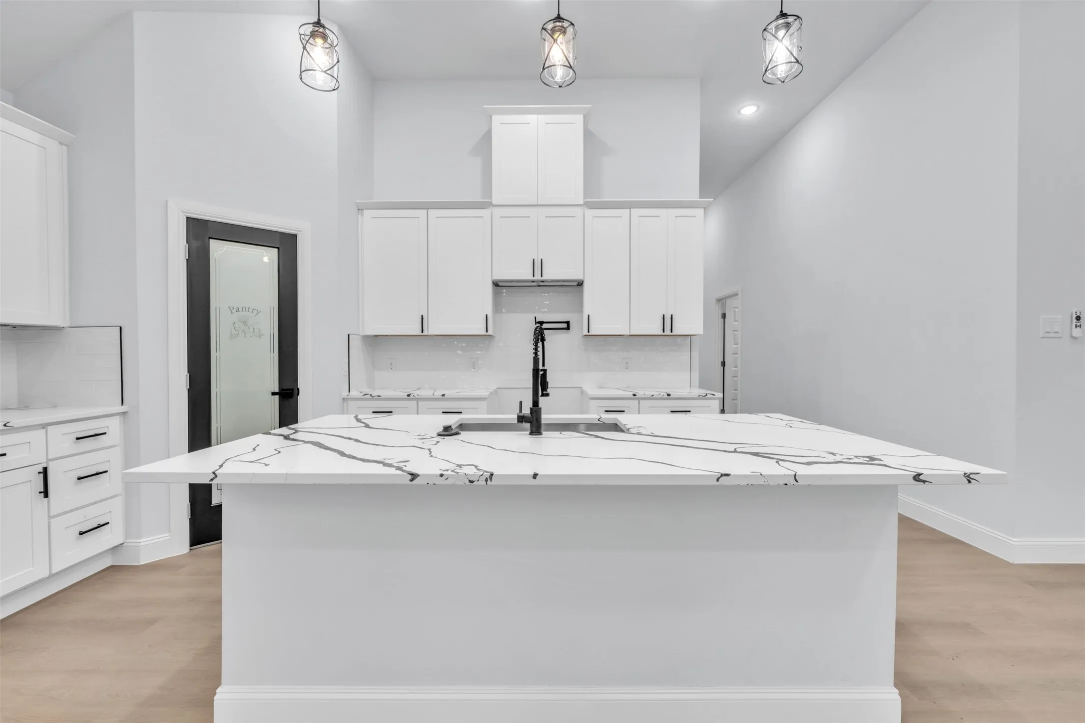 Kitchen featuring a large island with a patterned countertop, white cabinetry with dark hardware, a black faucet, and pendant lighting
