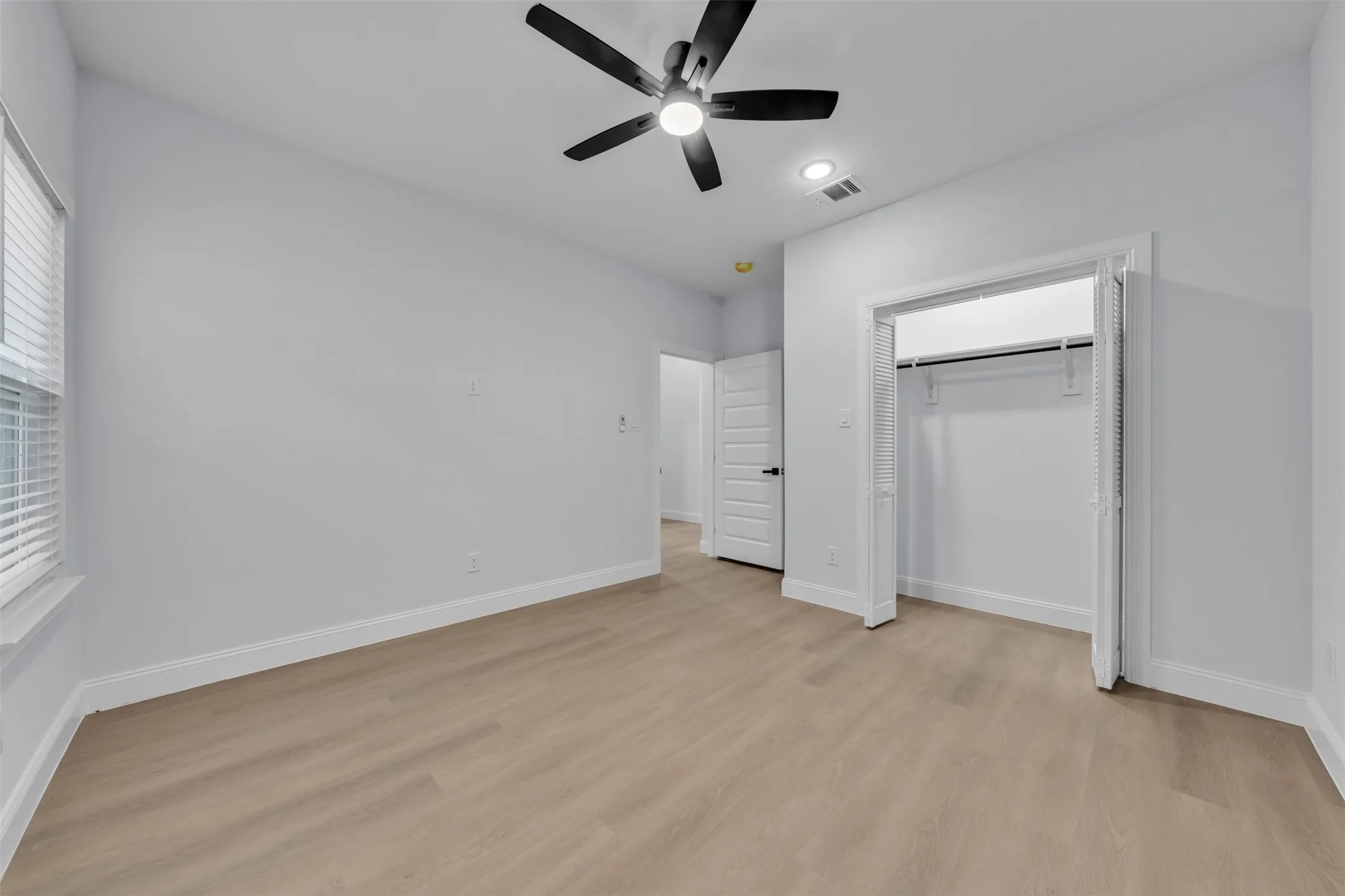 Spacious room featuring wood-finish flooring, light grey walls, and a contemporary ceiling fan with integrated lighting