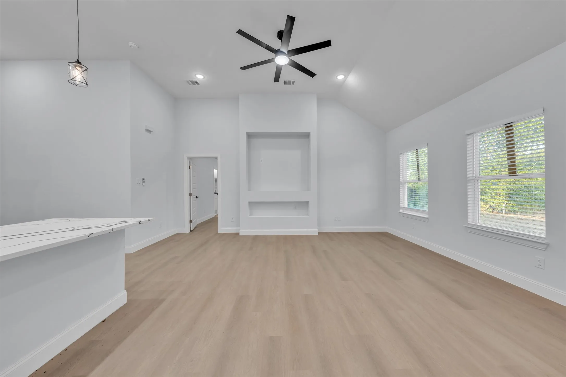 Spacious living area featuring light wood-finish flooring, vaulted ceilings, and a built-in media center