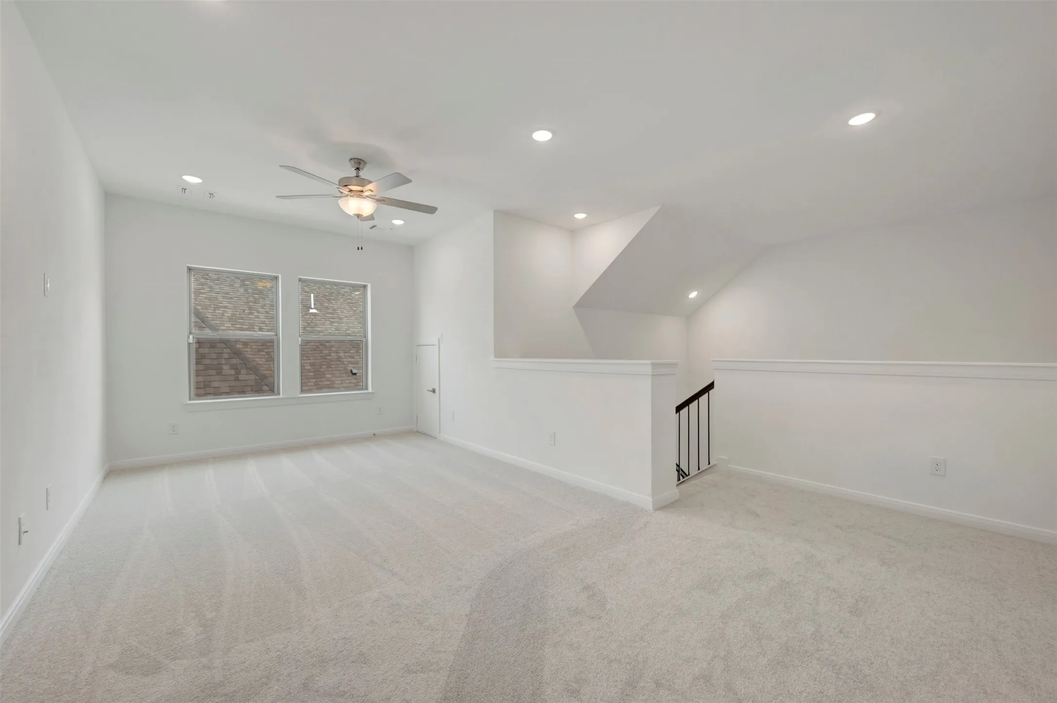 Expansive carpeted area featuring a ceiling fan, recessed lighting, and a staircase with an open wrought iron railing