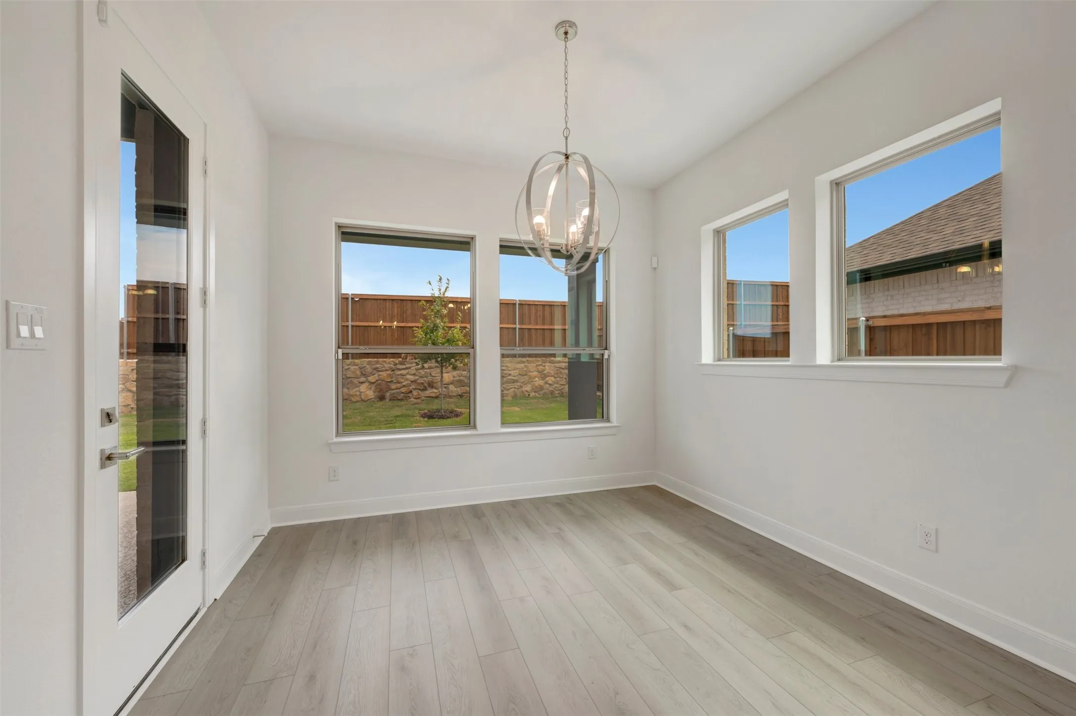 Spacious room featuring wood-finish flooring, multiple windows, a modern chandelier, and a glass-paneled exterior door