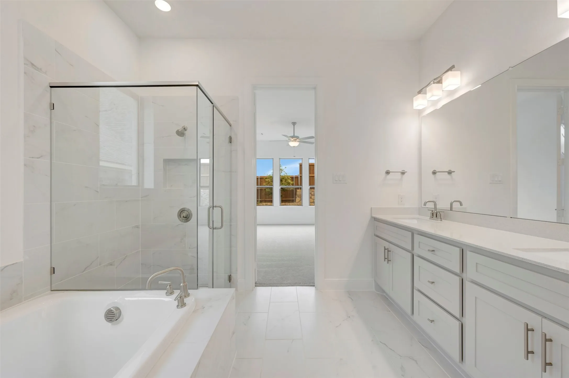 Freestanding bathtub with brushed nickel fixtures, glass-enclosed shower with tile surround, white dual vanity with undermount sinks, and polished chrome hardware