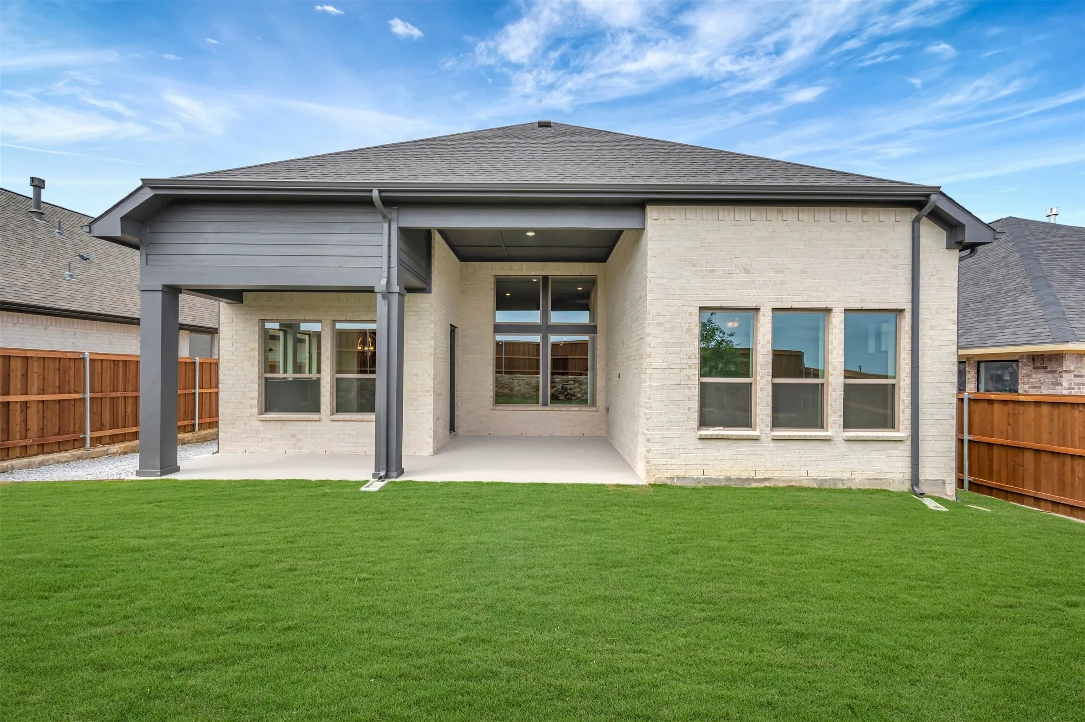 Expansive backyard featuring a manicured lawn, a covered patio, and light brick exterior
