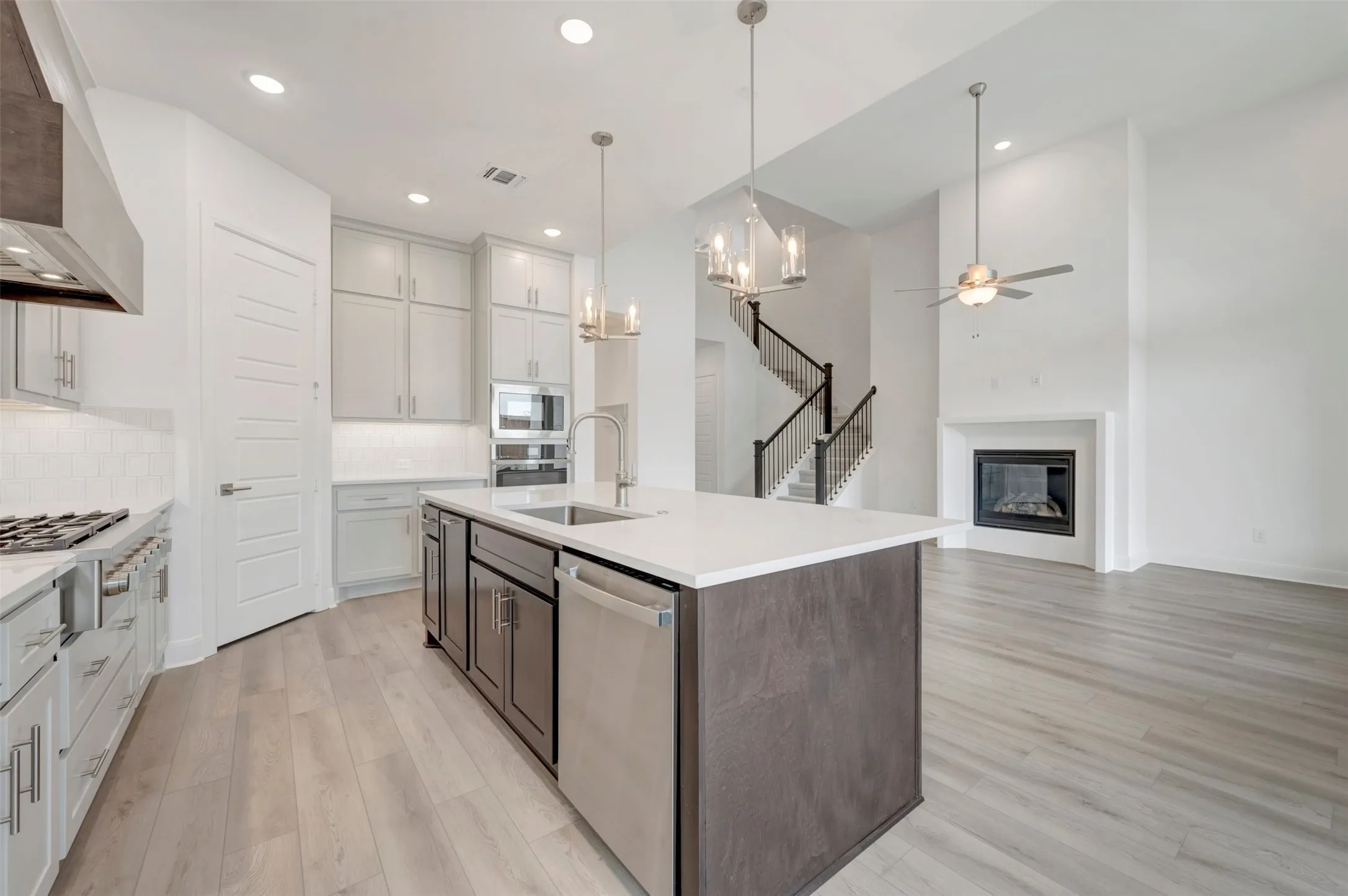 Expansive kitchen island with sink, stainless steel appliances, wood-finish flooring, built-in fireplace, and a two-story ceiling