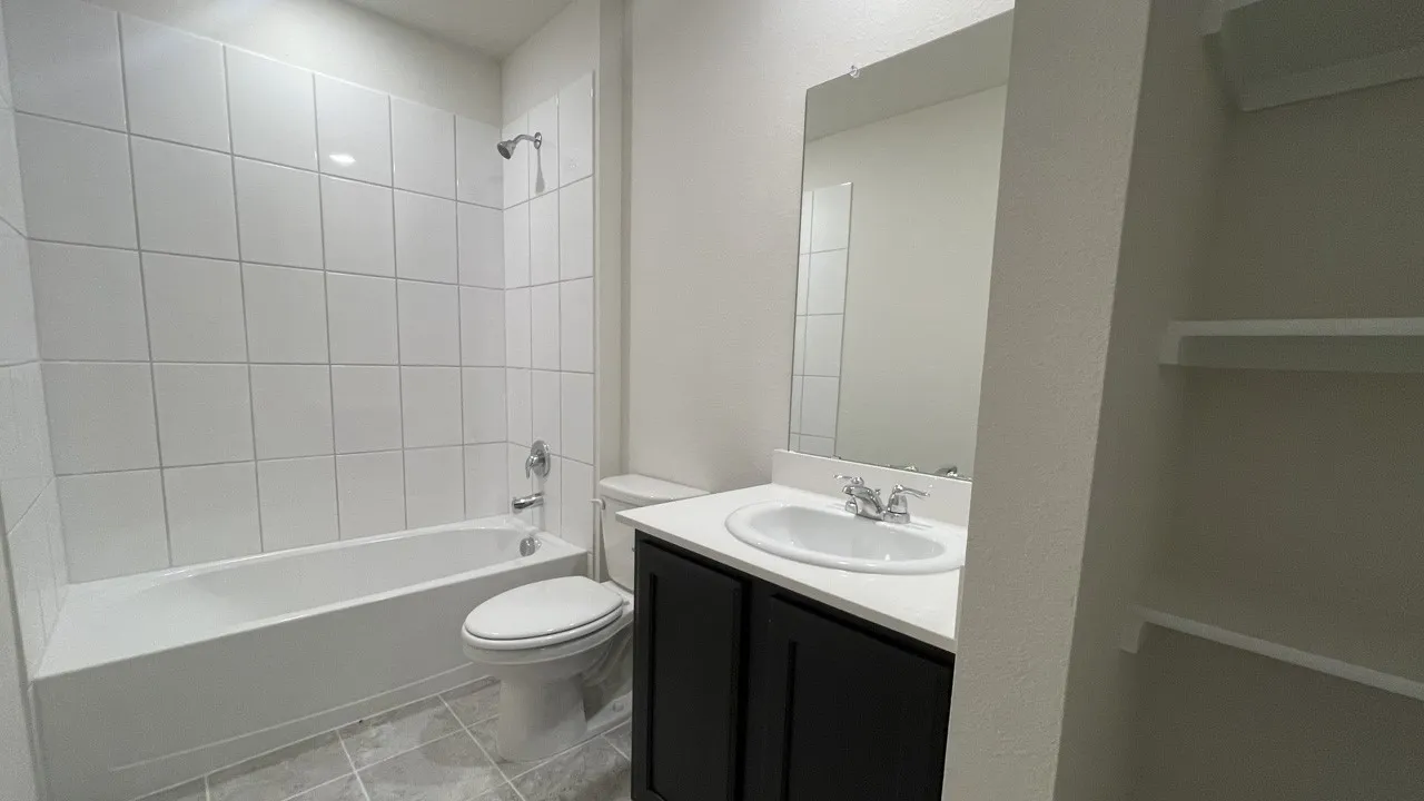 Contemporary bathroom featuring a tub-shower combination with white subway tile surround, a dark wood-finish vanity with an integrated sink and light-colored countertop, a large wall-mounted mirror, and tile flooring