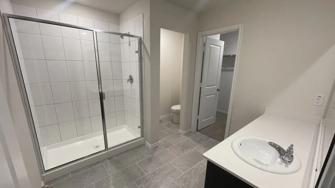 Bathroom featuring a spacious walk-in shower with tile surround and glass enclosure, a single vanity with an integrated sink and chrome faucet, and large format floor tiling