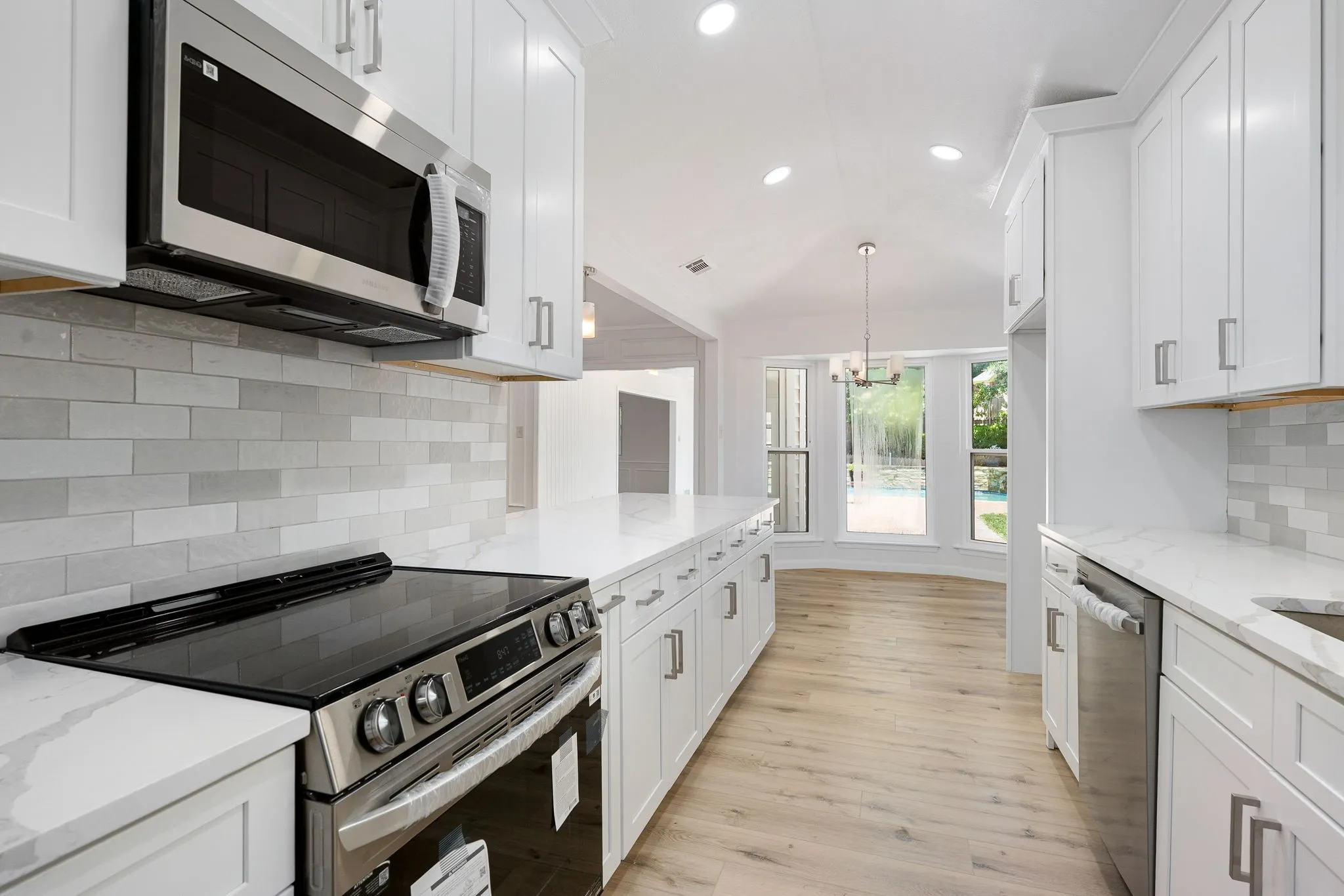 Updated kitchen featuring white shaker cabinetry, stainless steel appliances, light-toned wood-finish flooring, and a subway tile backsplash
